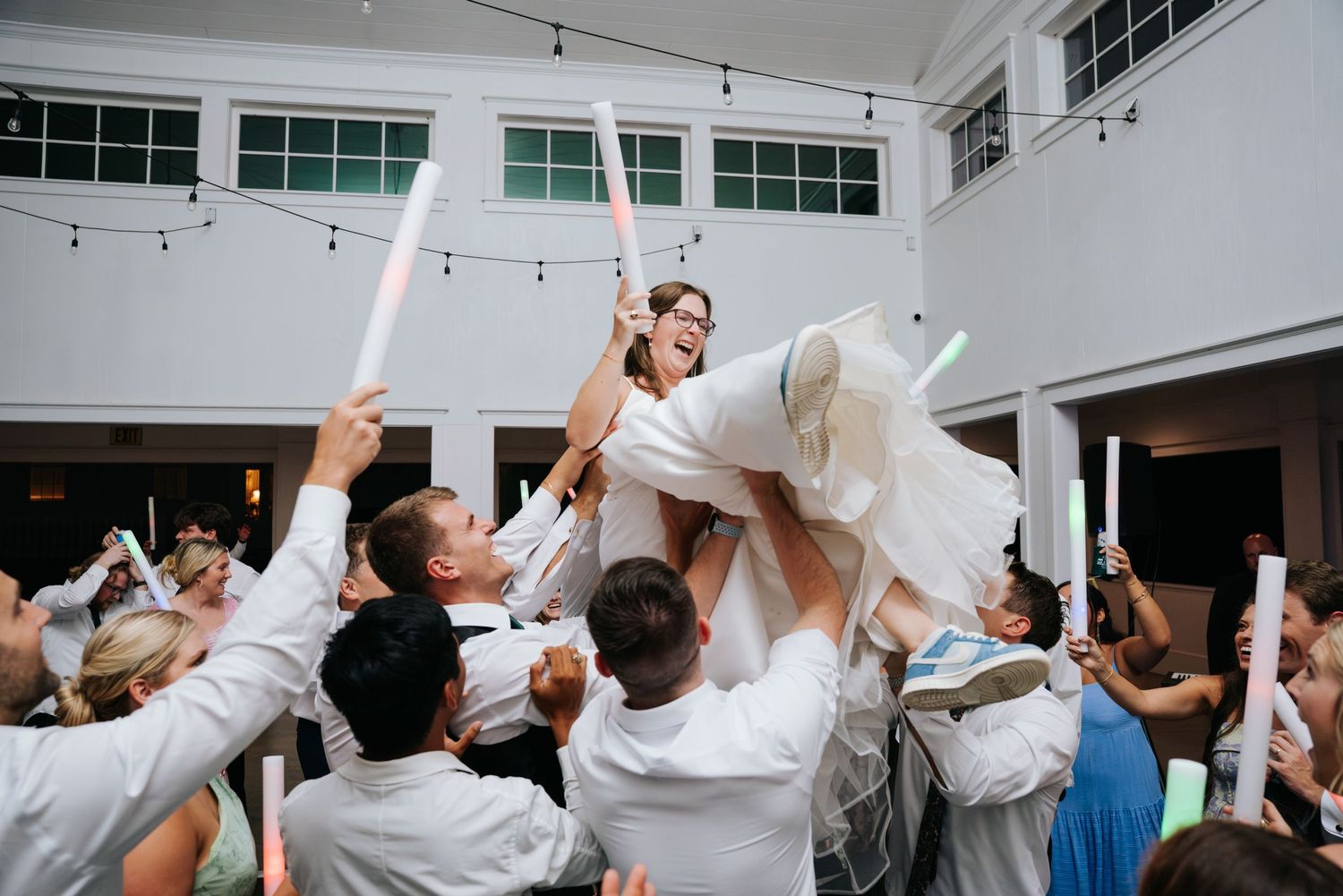 Wedding celebration with guests lifting someone in a white dress during a joyful reception moment.
