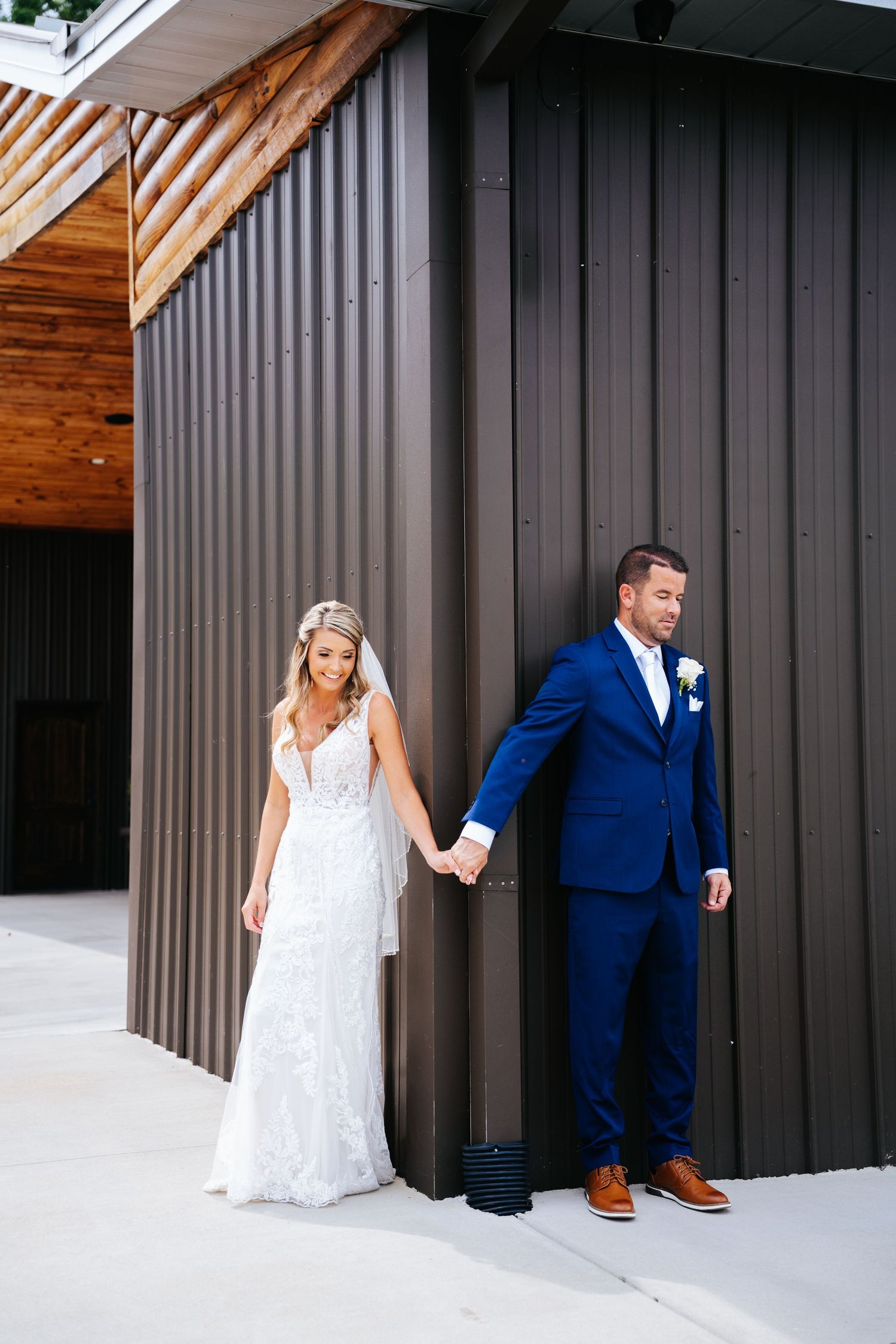 Playful wedding couple poses against modern grey wall in formal attire.