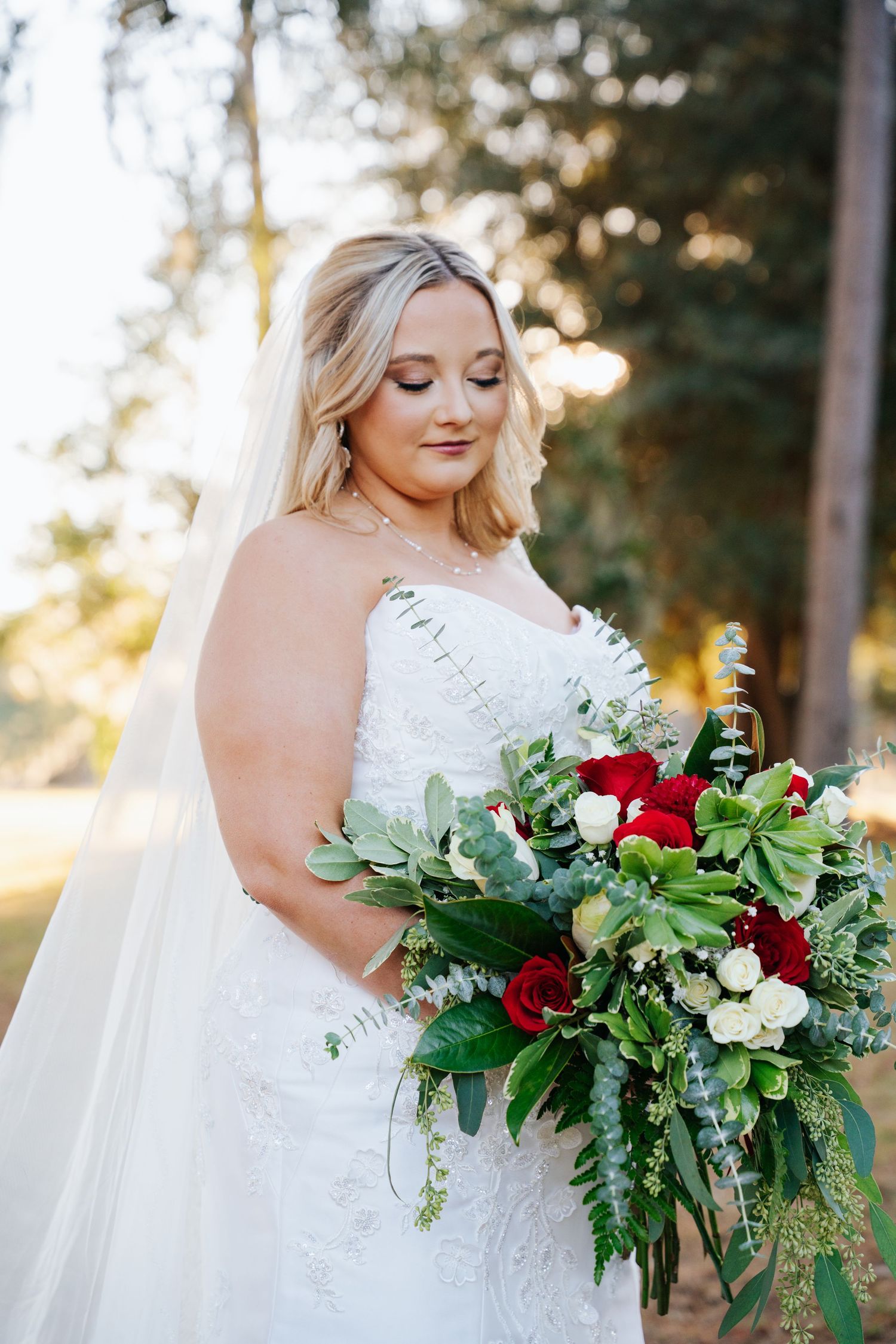 Bride in lace wedding dress holds lush burgundy and green bouquet with eucalyptus during golden hour photography session.