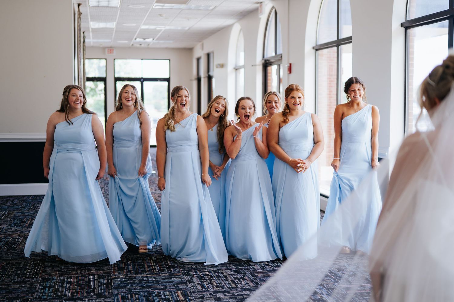 Bridesmaids in light blue dresses line up in an elegant indoor venue.