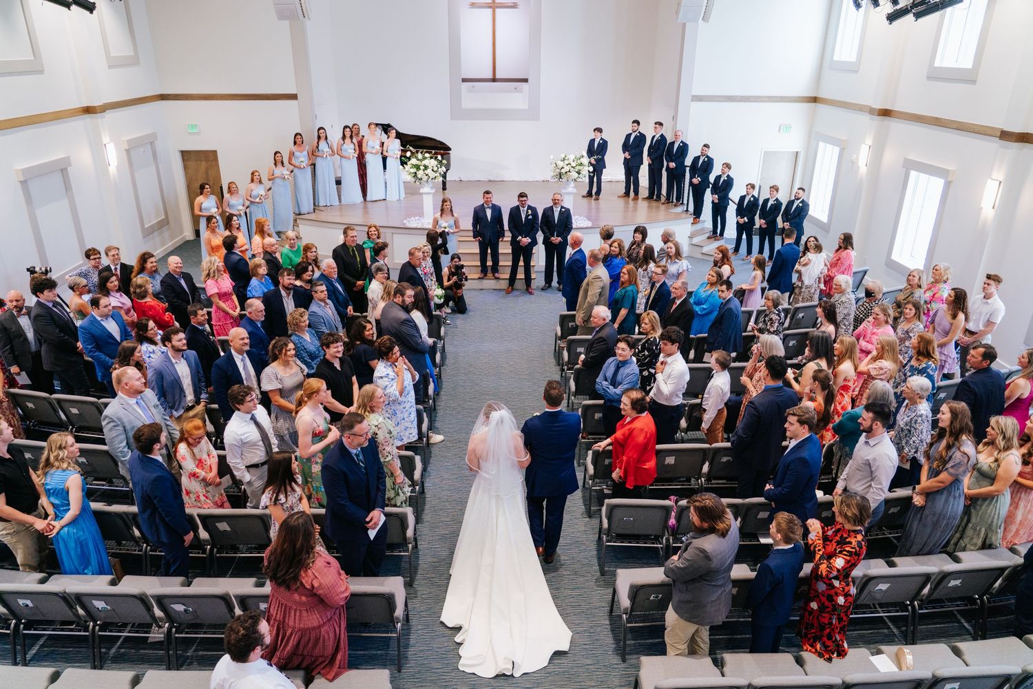 Wedding ceremony in a bright church sanctuary with guests seated in wooden pews.