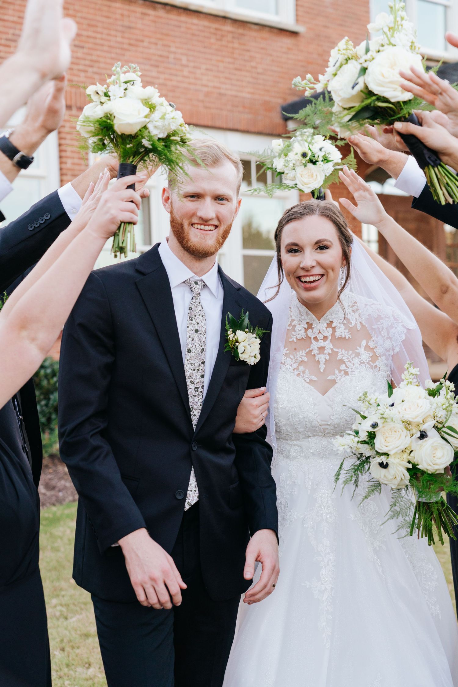 Wedding couple shares joyful moments with their wedding party outside a brick building.