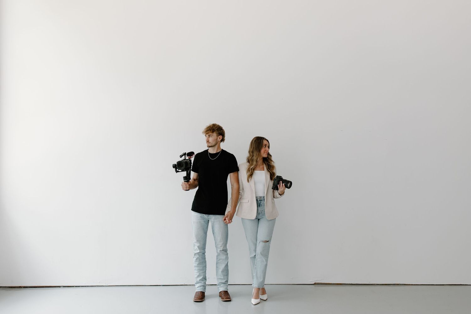 Two photographers in casual attire standing against a white studio wall.