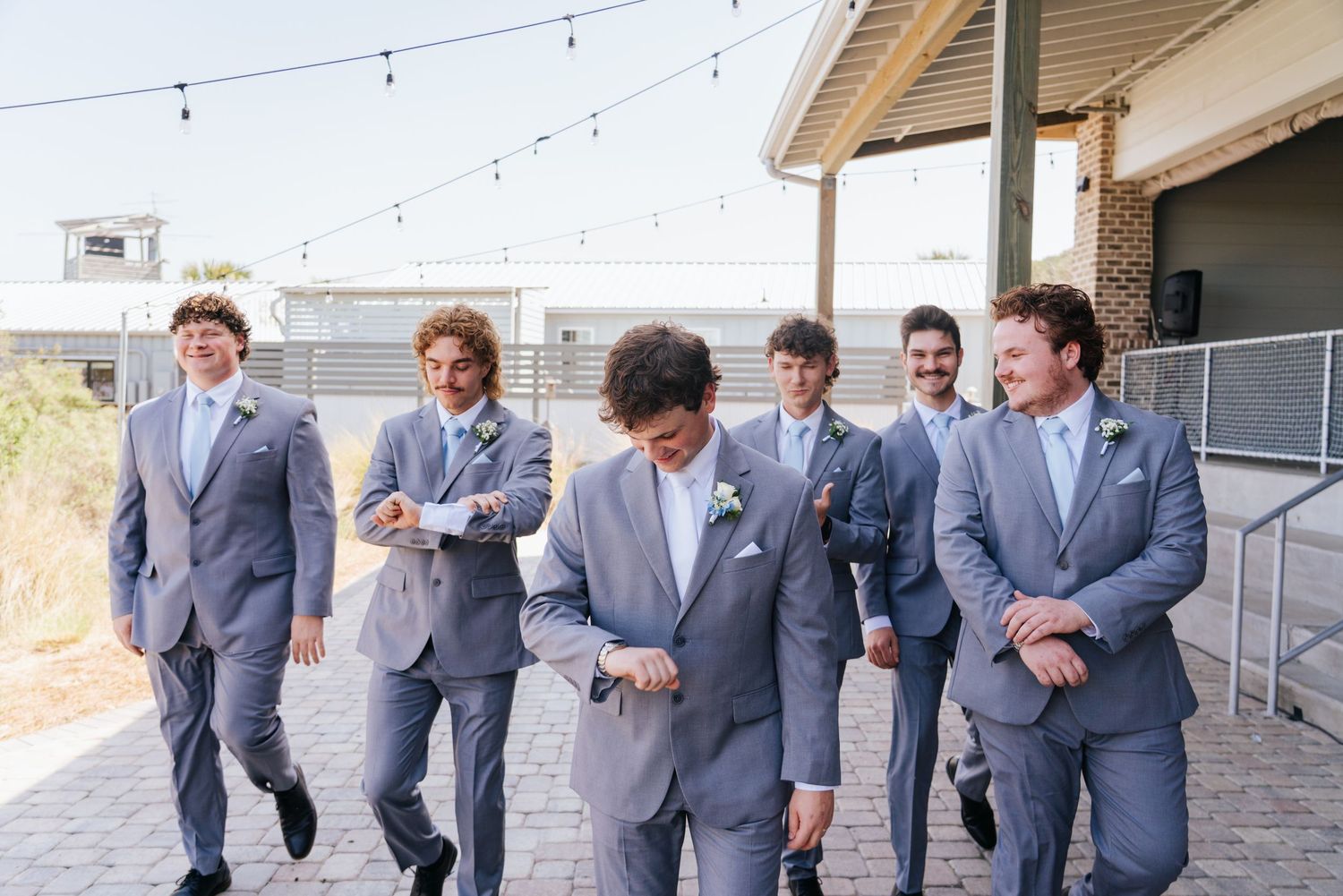 Groomsmen in gray suits walking and laughing together at an outdoor venue.