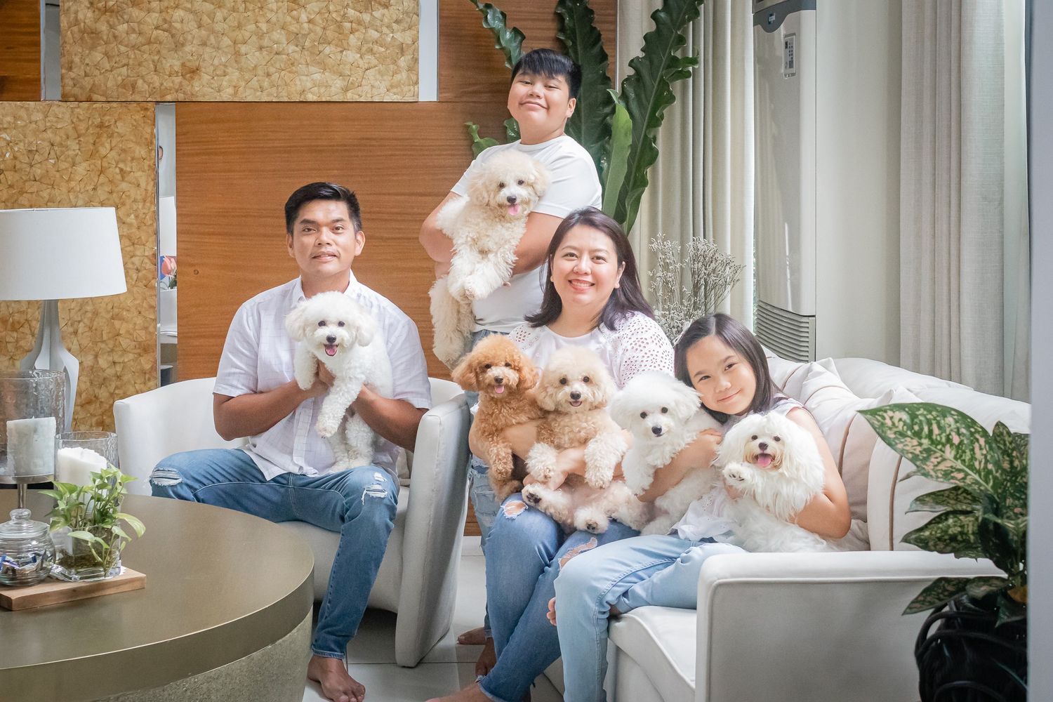 People seated on white furniture holding small white dogs in a modern apartment space.