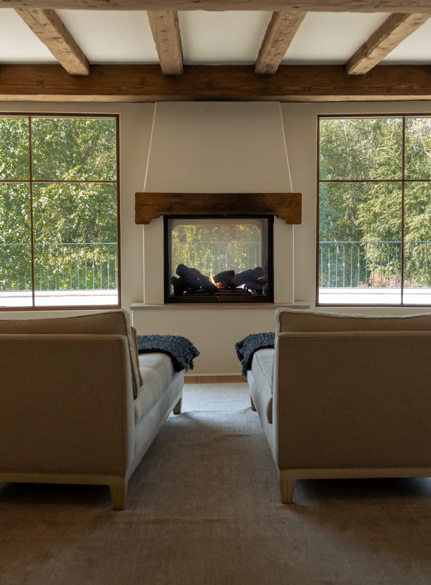 Modern spa room with exposed beam ceiling, fireplace and large windows overlooking nature.