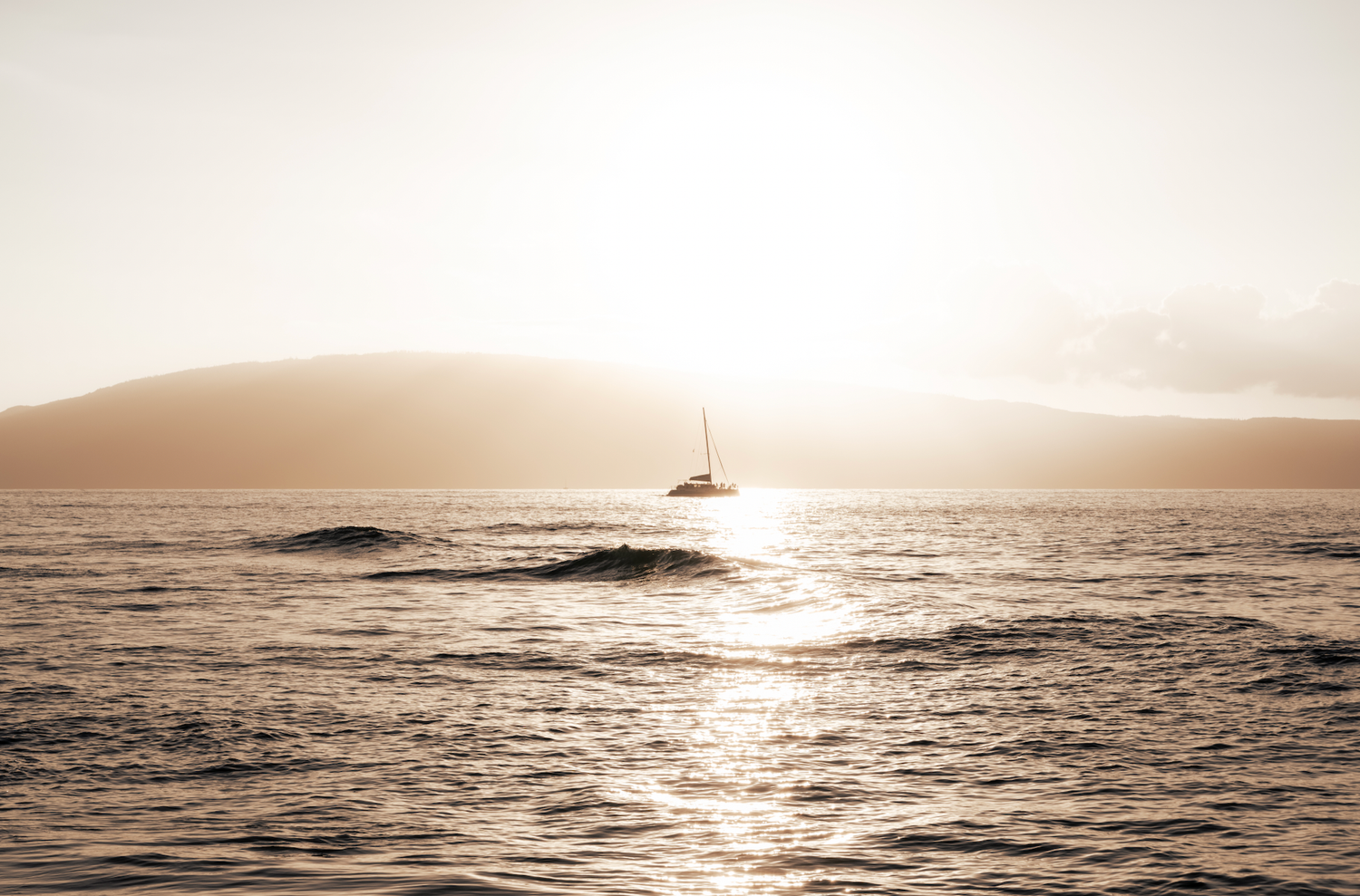 A peaceful seascape at sunset with a silhouetted boat on the horizon in Maui.
