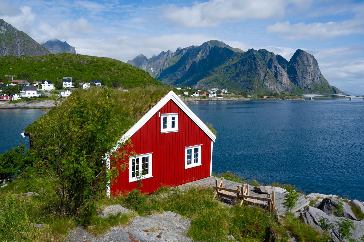 A bright red cabin perched on a rocky coastline with dramatic mountain views in Lofoten, Norway.