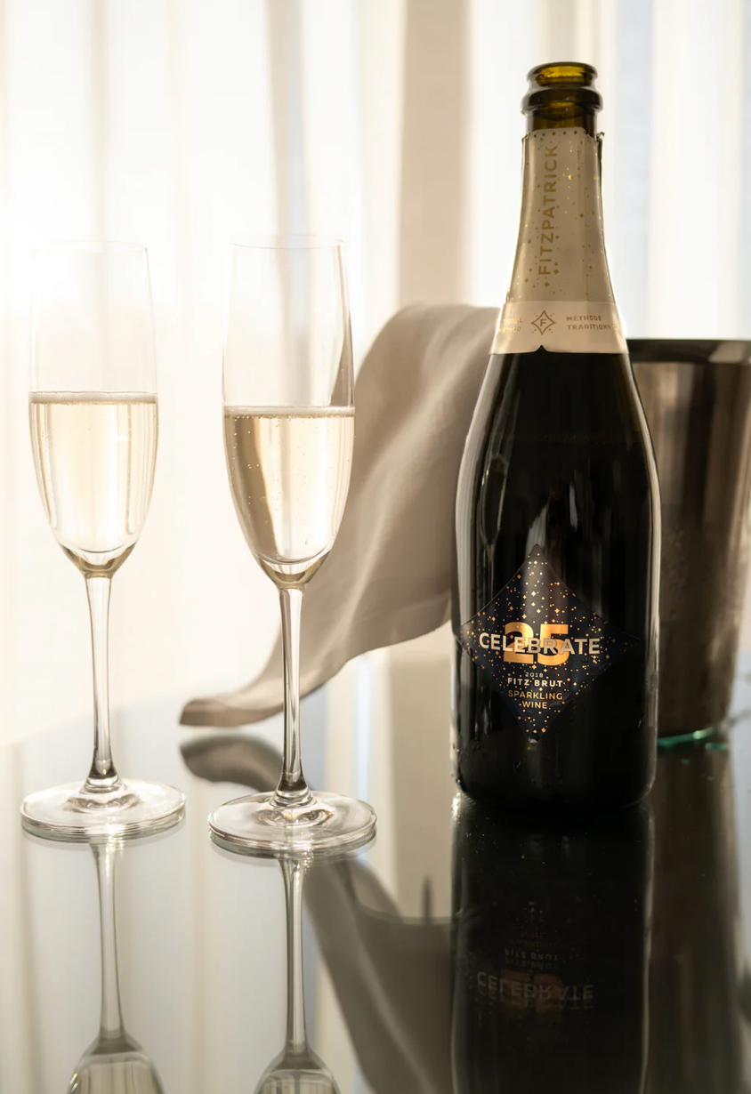 Champagne bottle with two glasses on reflective surface against white curtain background.