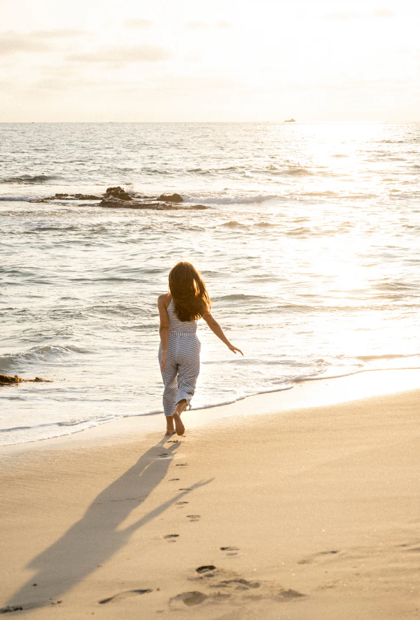 Woman walking along beach at sunset leaving footprints in golden sand.