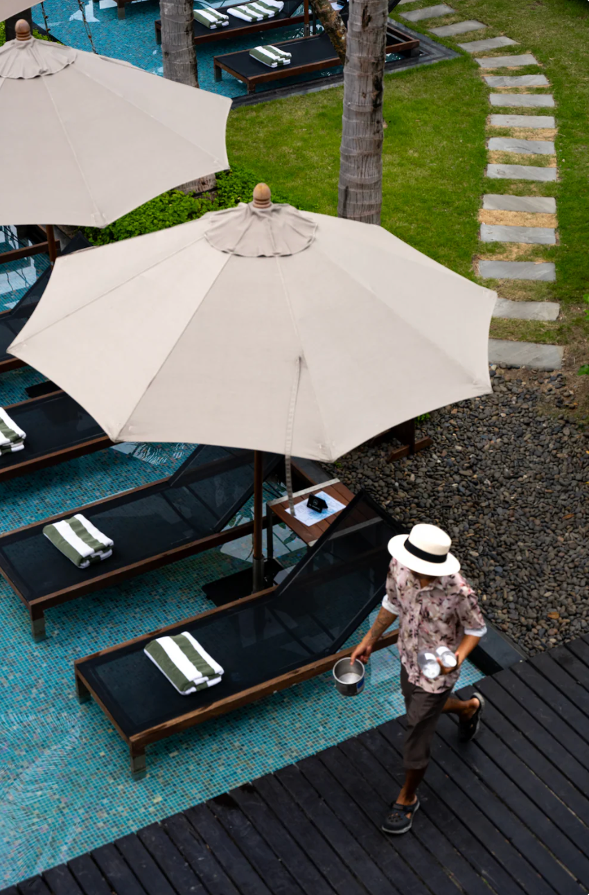 White beach umbrella and lounge chairs beside a swimming pool with curved stone pathway in Koh Samui, Thailand.