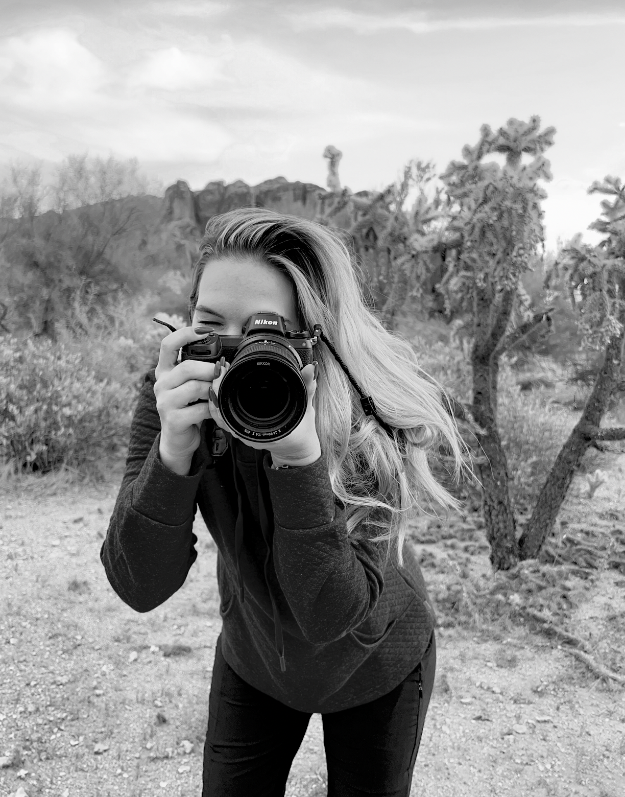 Black and white photo of a photographer using a professional DSLR camera in an outdoor nature setting.
