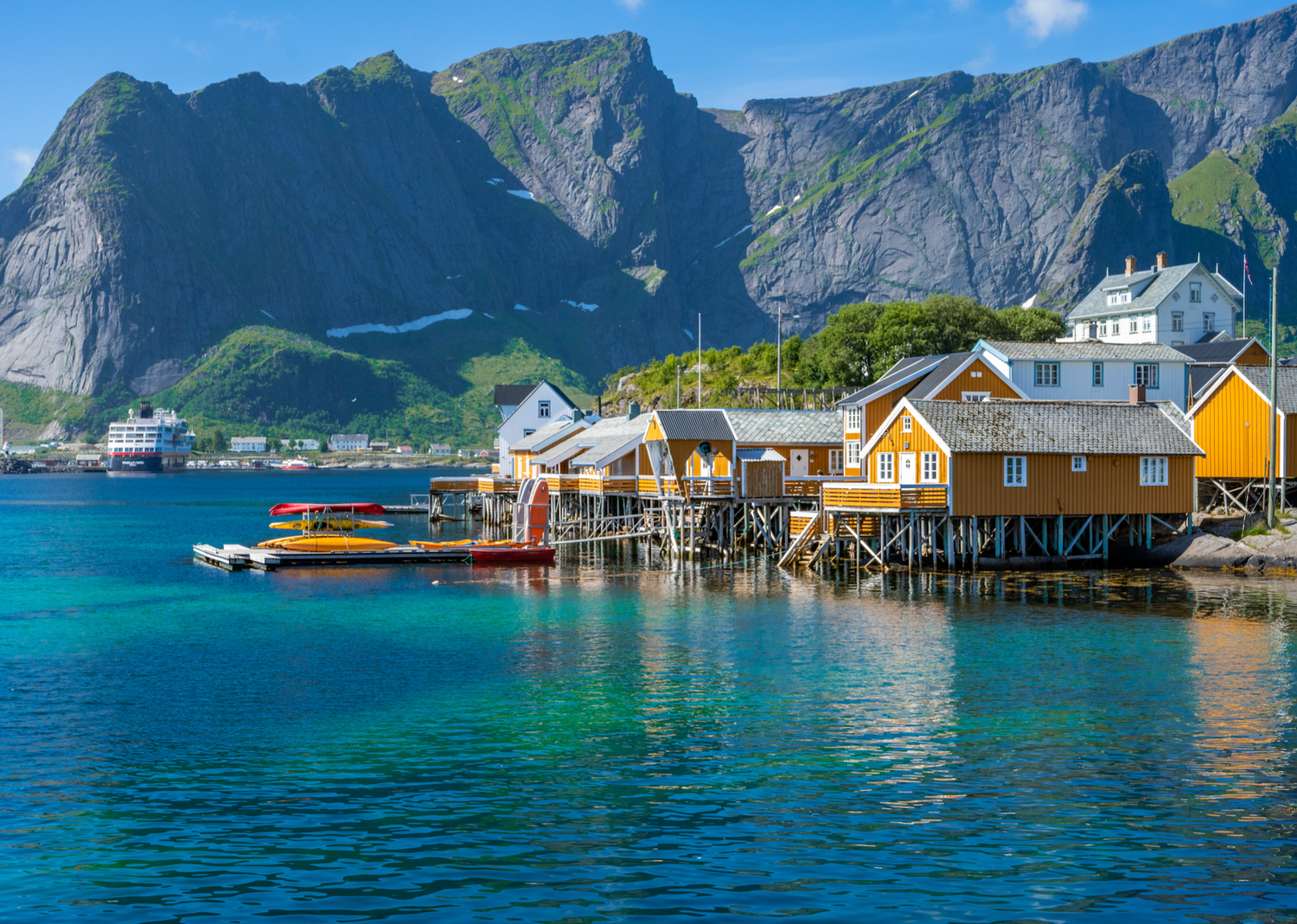 Yellow wooden fishermen's houses on stilts along a Norwegian fjord with dramatic mountain backdrop.