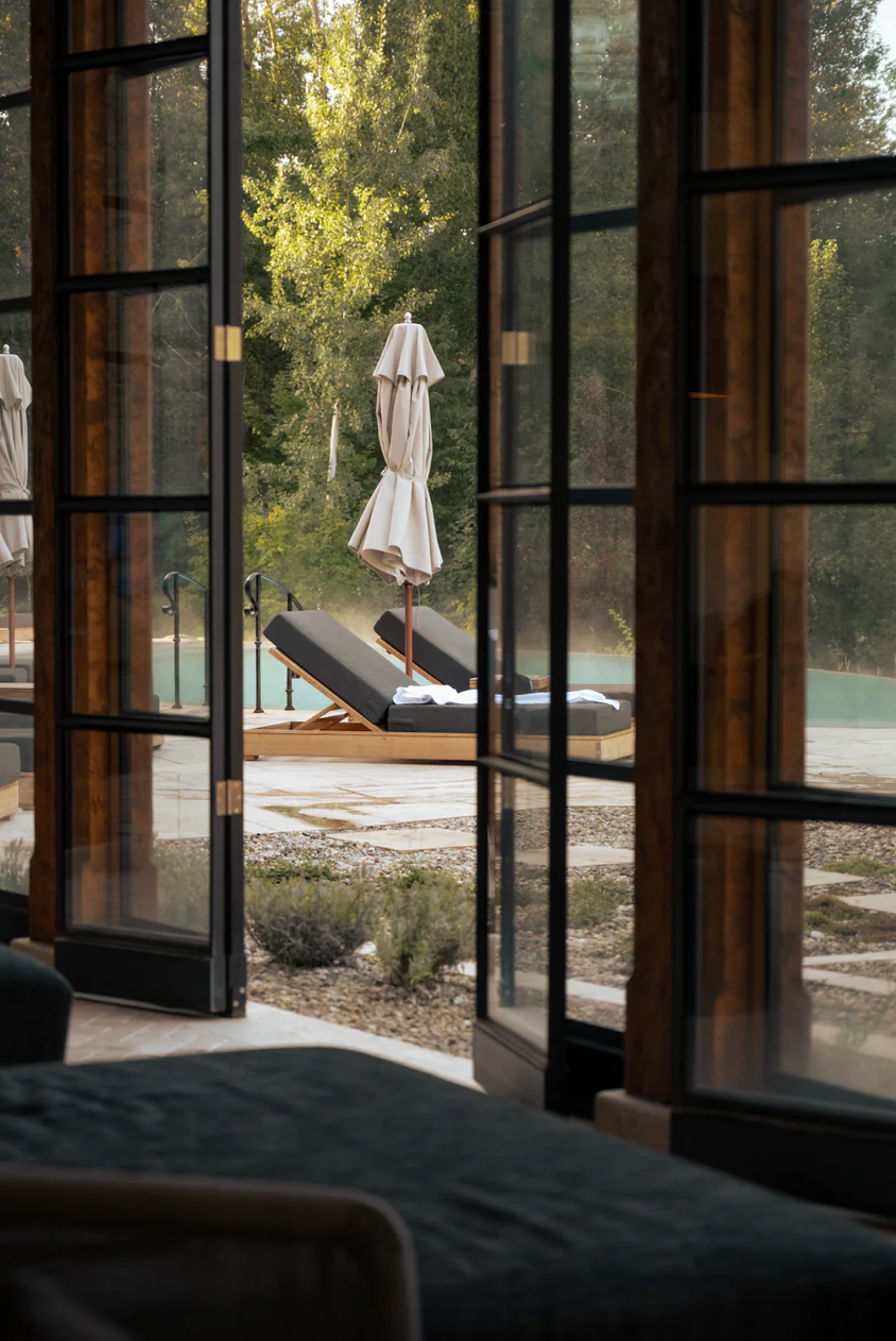 Modern poolside lounge area with glass windows and white umbrellas in natural daylight.