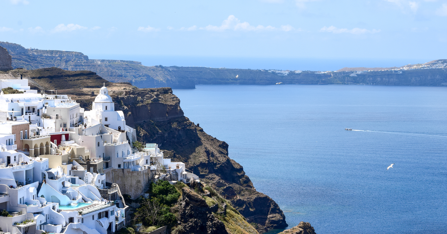 White buildings cascade down the cliffs of Santorini overlooking the blue Mediterranean Sea.