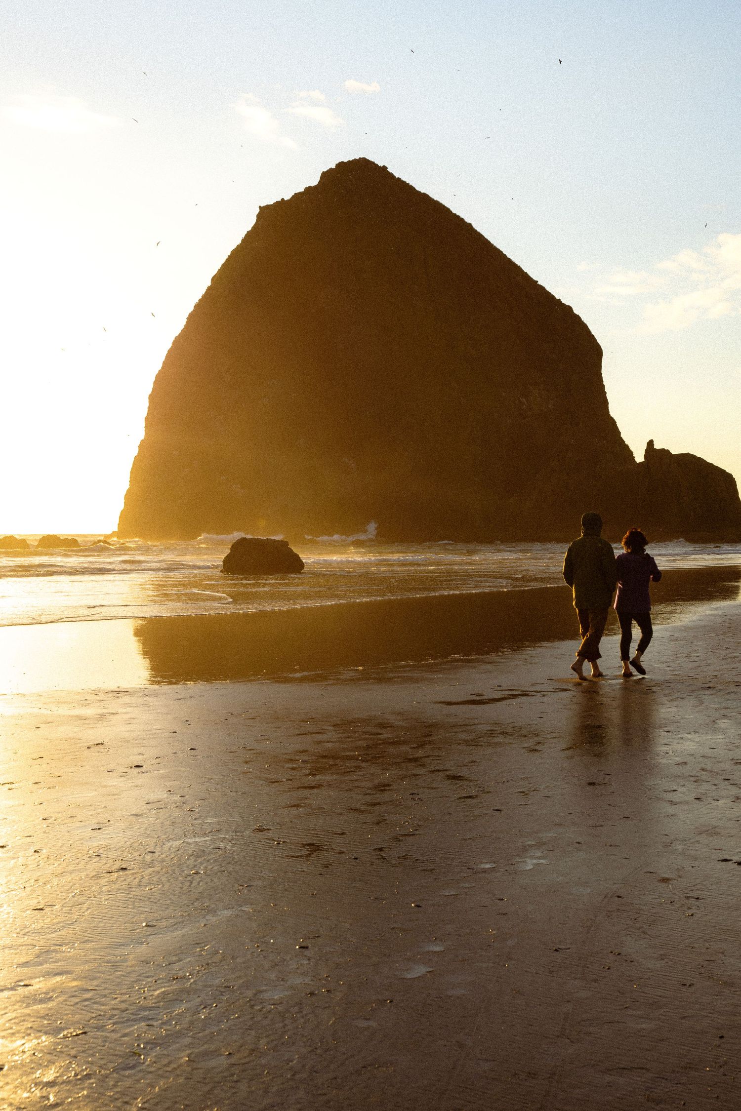 Silhouetted couple walking on beach at sunset near Haystack Rock in Cannon Beach, Oregon.