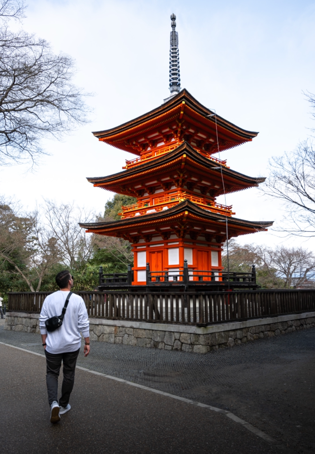 Traditional red Japanese pagoda temple against cloudy sky with bare winter trees.