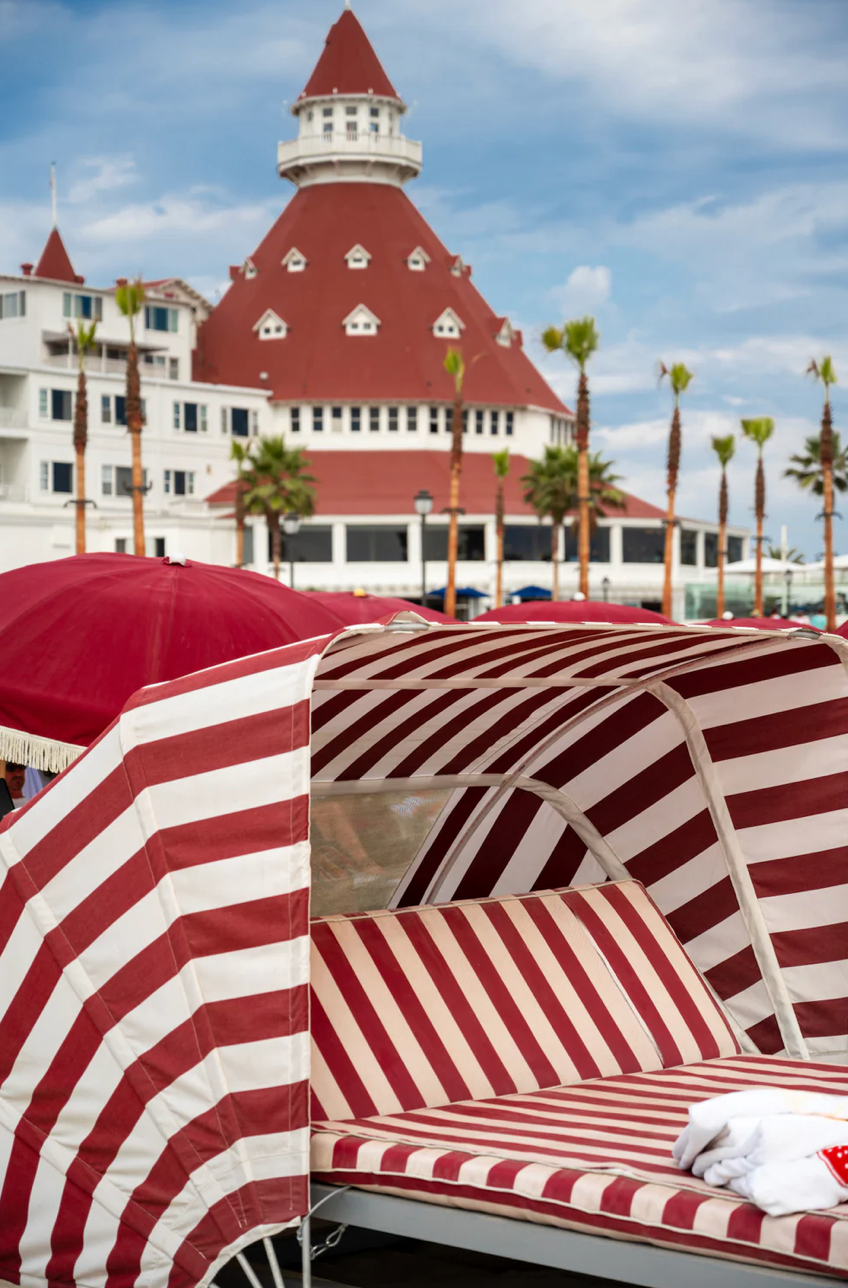Red and white striped beach umbrellas with historic Hotel del Coronado in background.