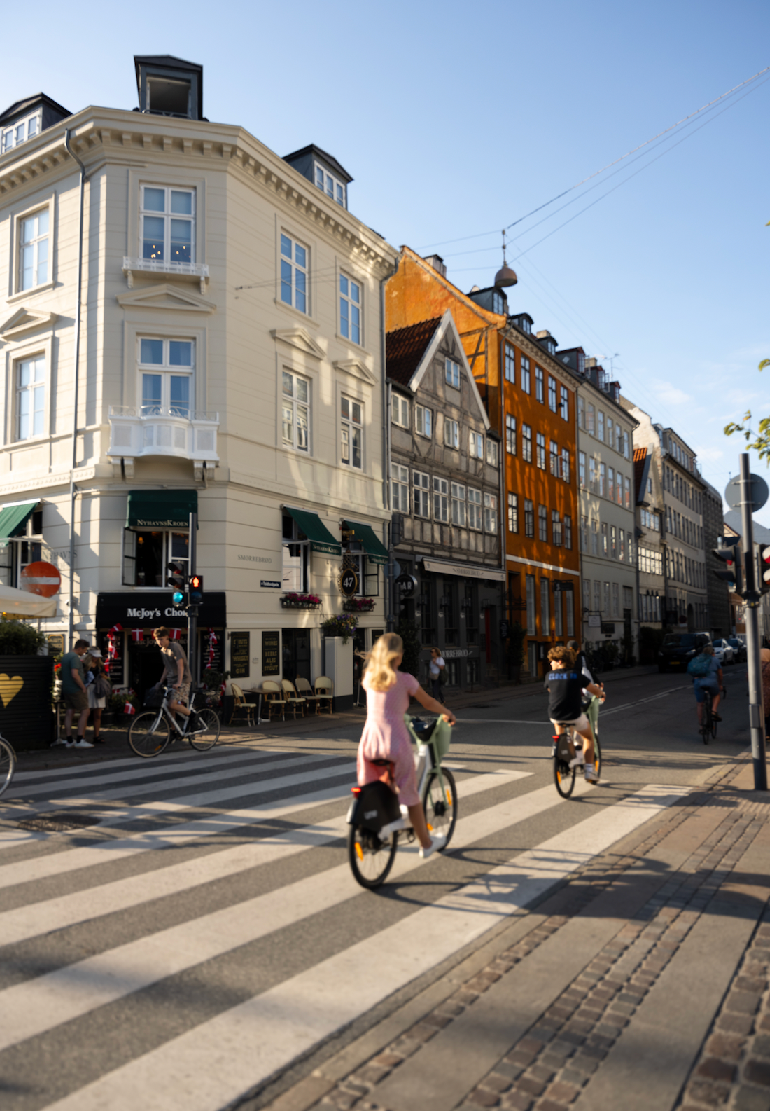 Historic colorful buildings line a bustling city street with cyclists in Copenhagen.