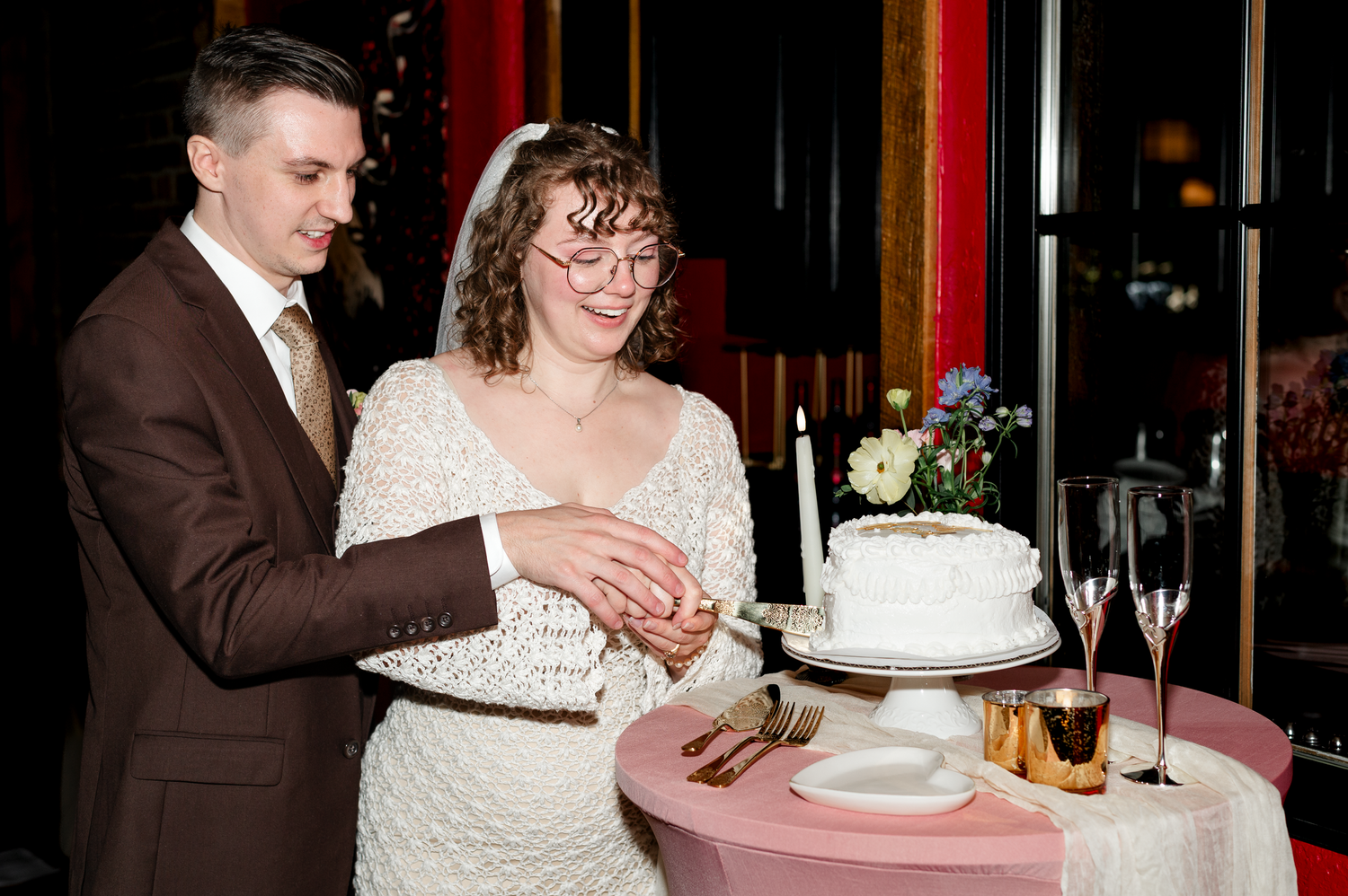 Wedding couple cutting cake at reception with champagne glasses and candles.
