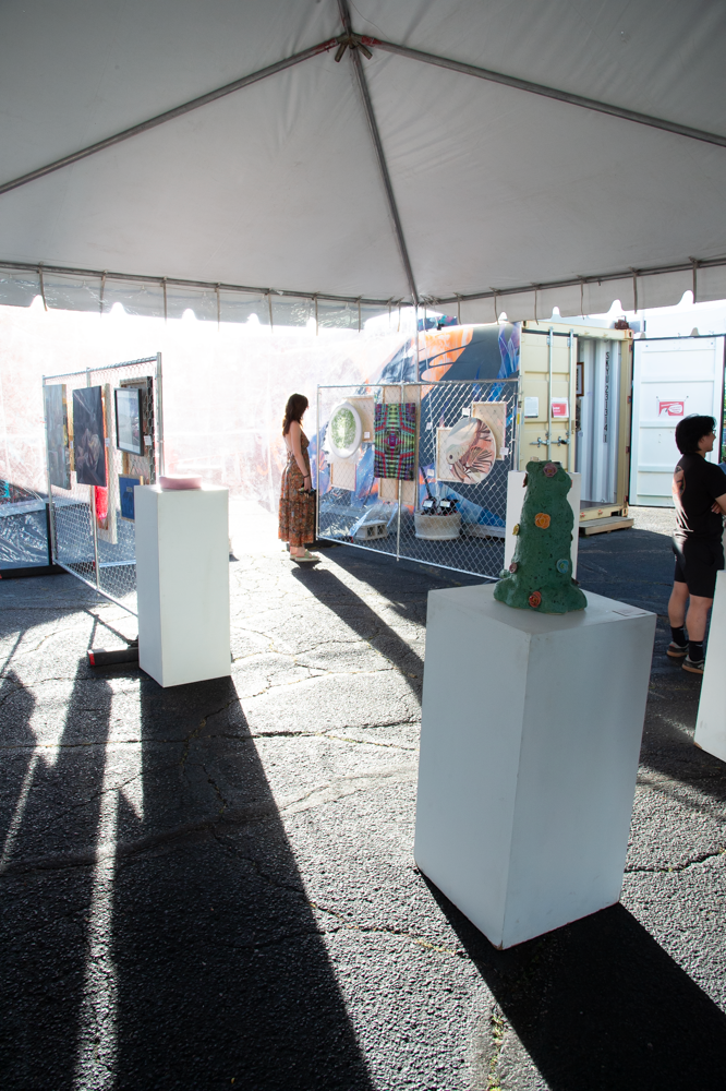 Art installation displayed on white pedestals under a tent with long shadows cast on the ground.