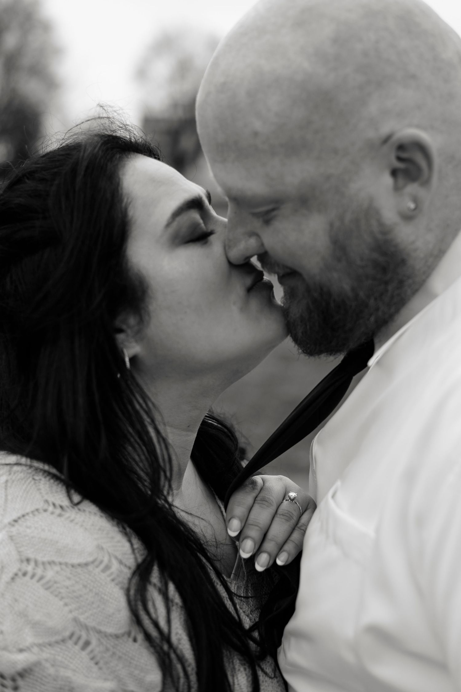 Black and white photo of a couple sharing a romantic kiss, woman in lace dress holding man's tie.