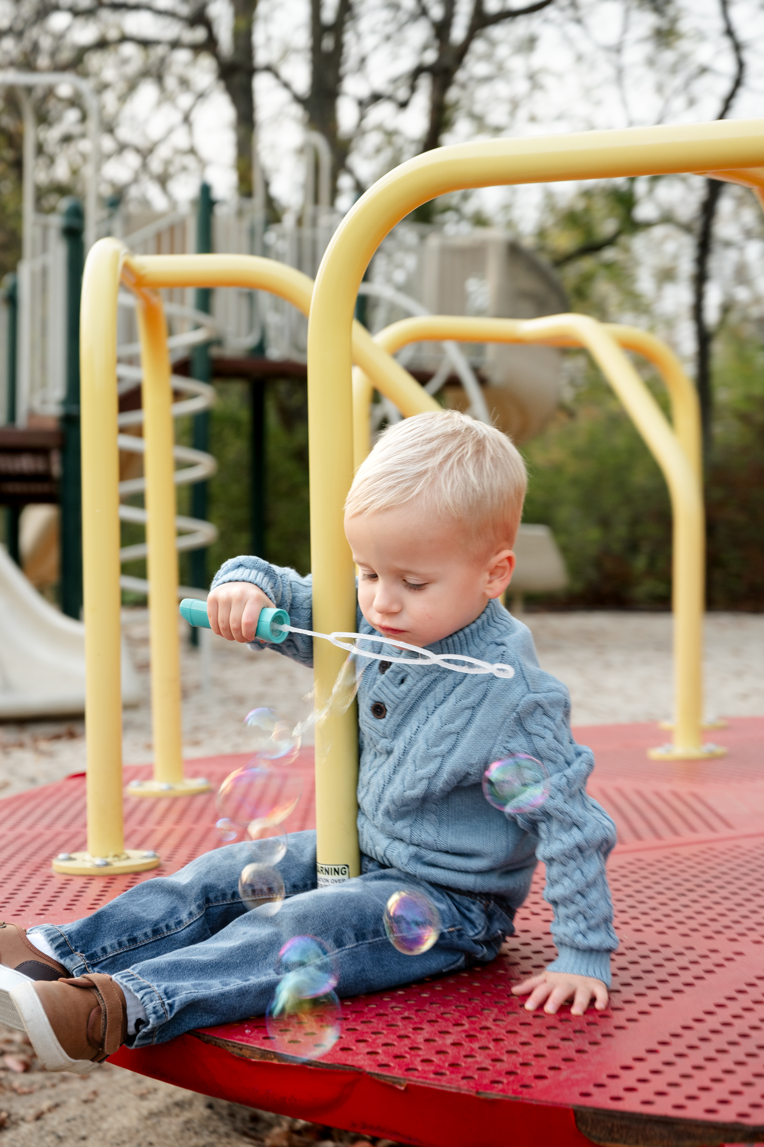 A child in denim plays on a red playground platform on an autumn day.