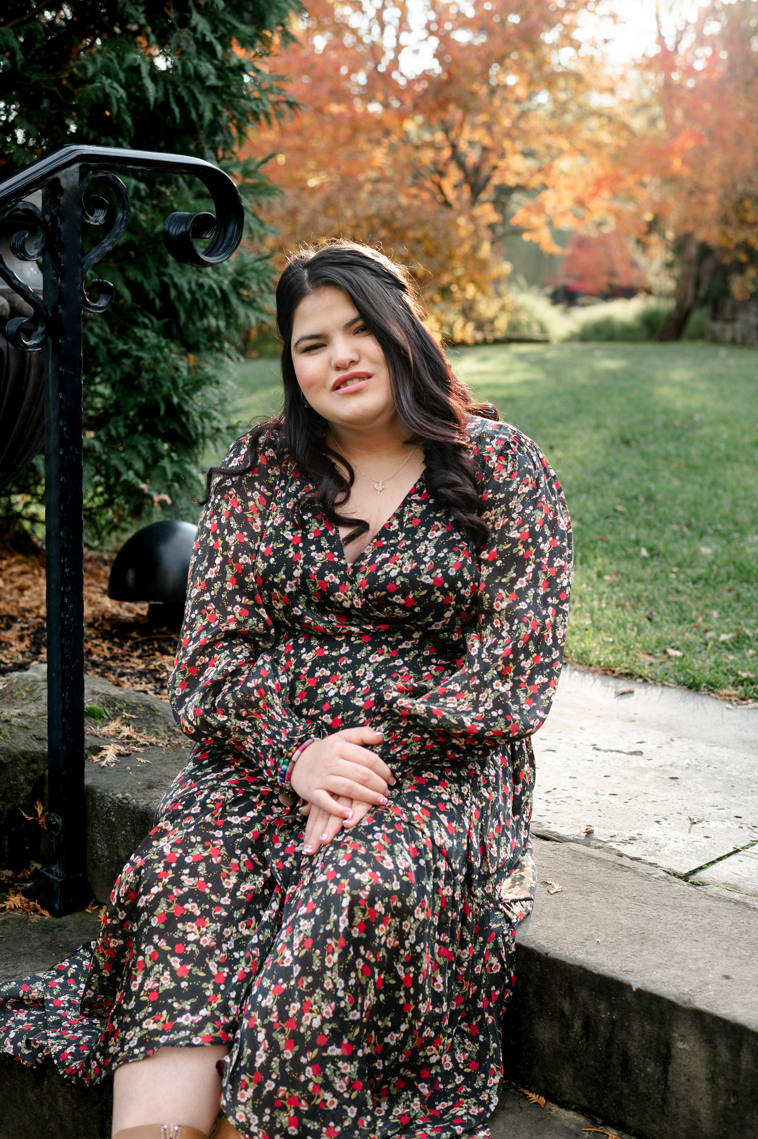 A floral dress photoshoot in a park during autumn with colorful fall foliage in the background.