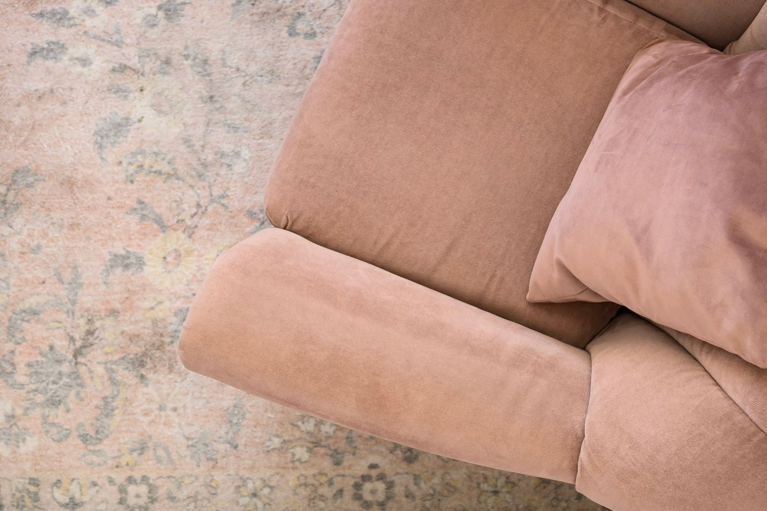 A modern beige velvet sofa with plush cushions and clean lines sits against a textured wall.