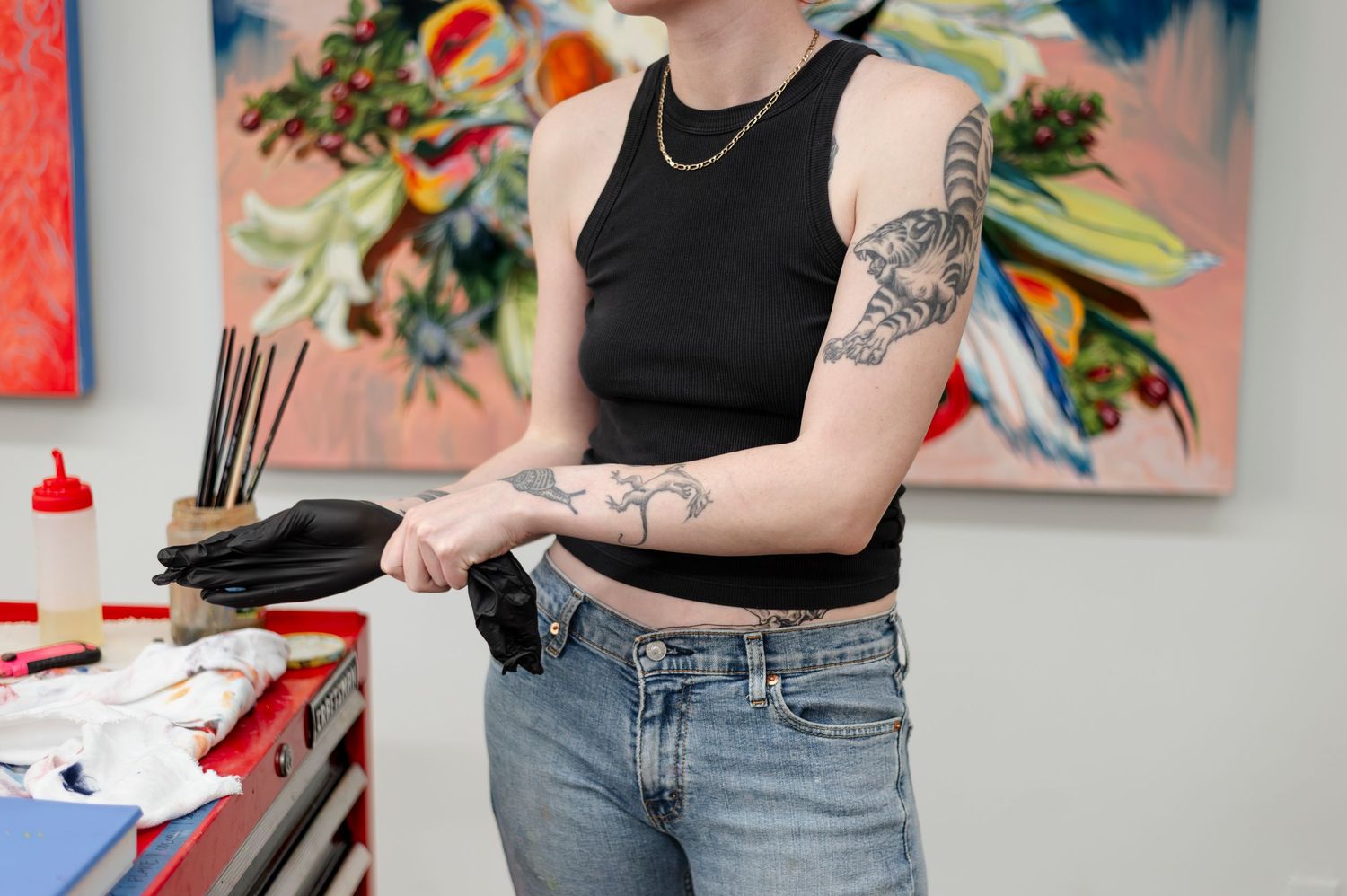 Person in black tank top and jeans holding sneakers in front of colorful wall art display.