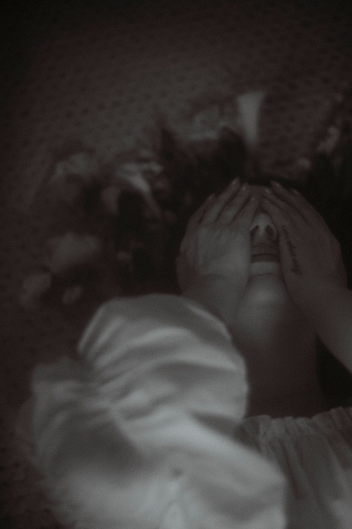 Woman covering face with hands lying down, dark moody overhead fine art portrait photography.