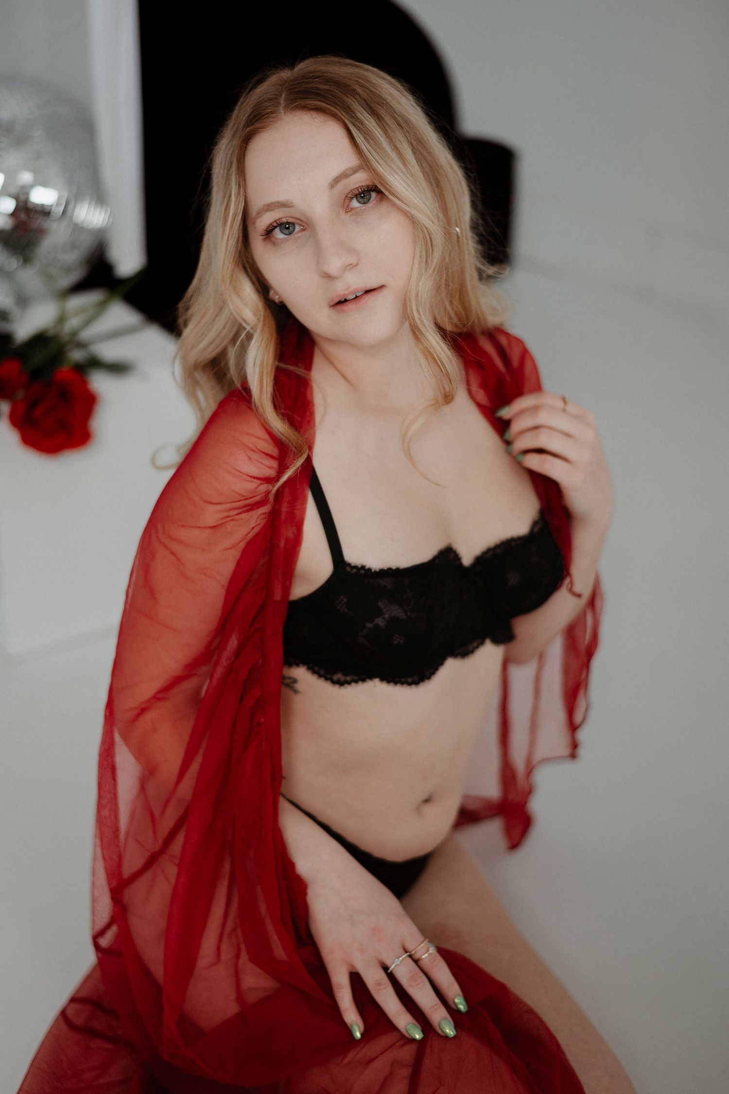 Intimate boudoir photo with red sheer robe and black lingerie against light background with roses.