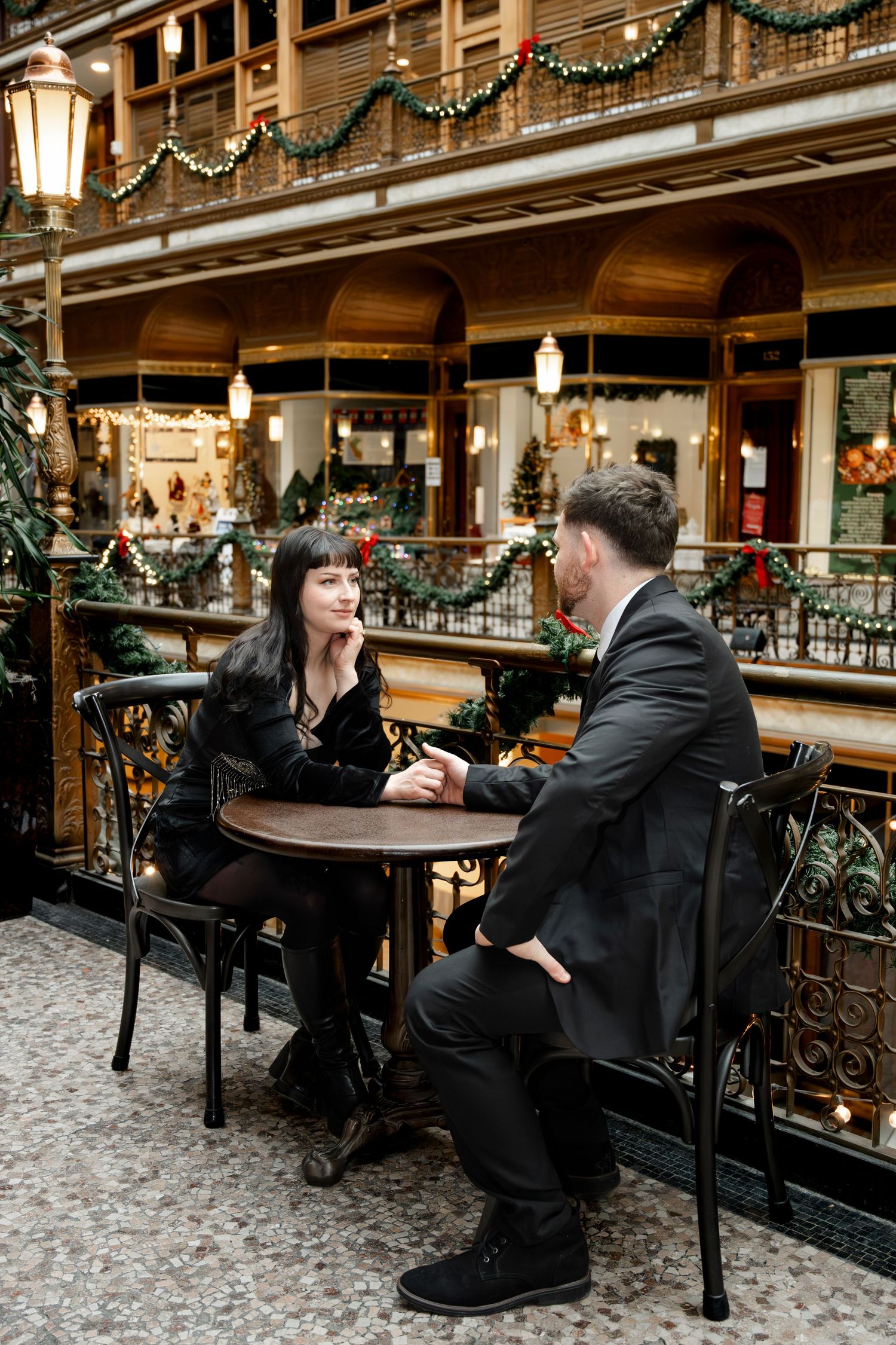 Couple in black attire sitting at a round table in a festive holiday decorated indoor arcade.