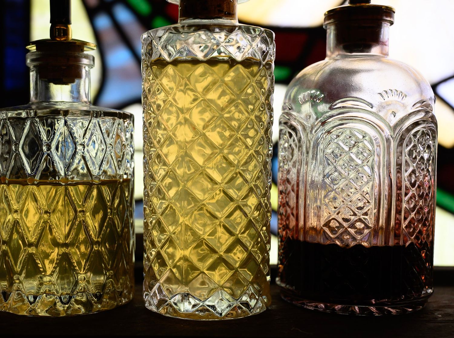 Vintage cut glass tumblers and decanters with ornate diamond and geometric patterns displayed in a row.
