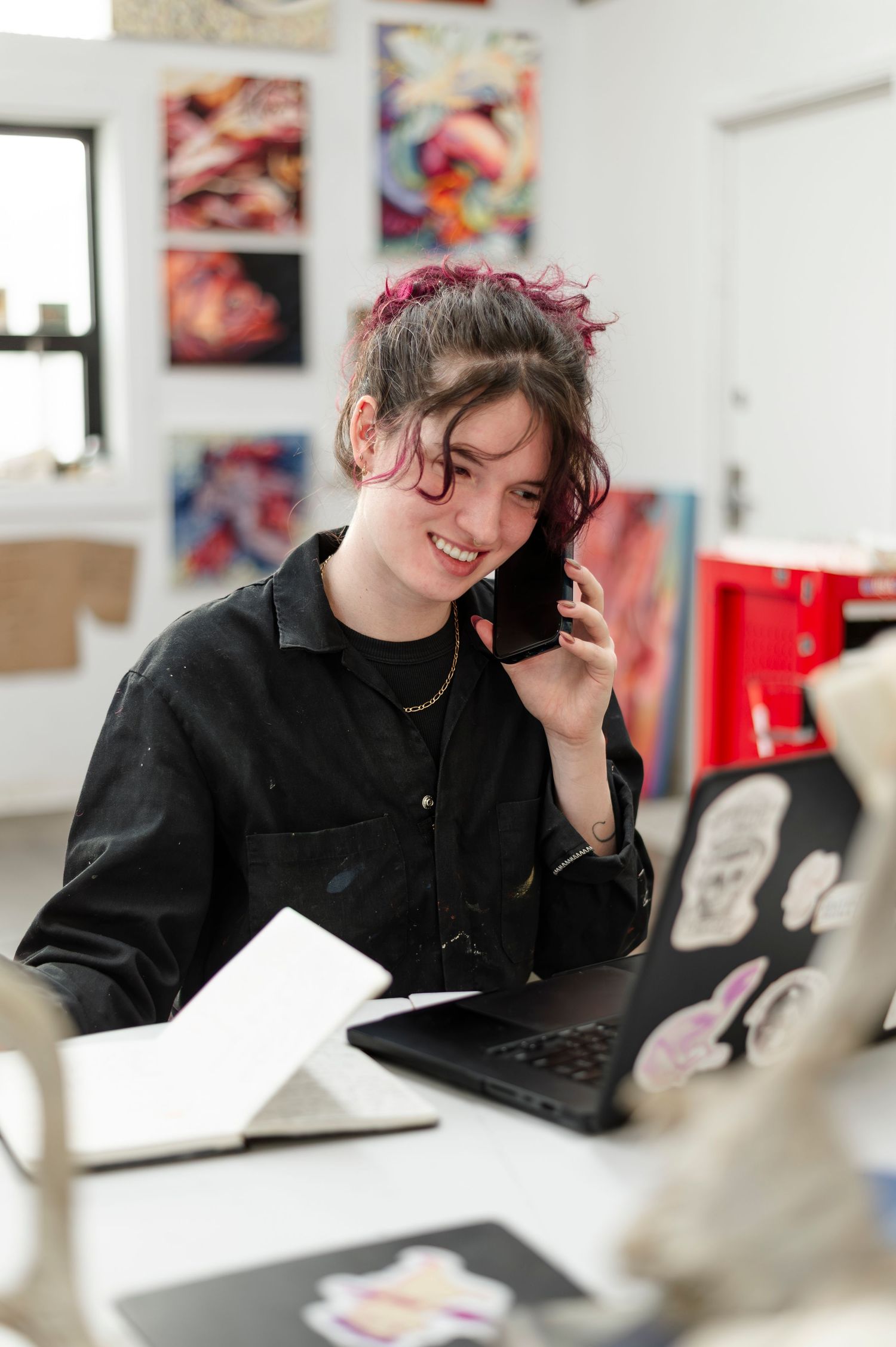Professional working on laptop in bright creative studio with colorful artwork displayed on walls.