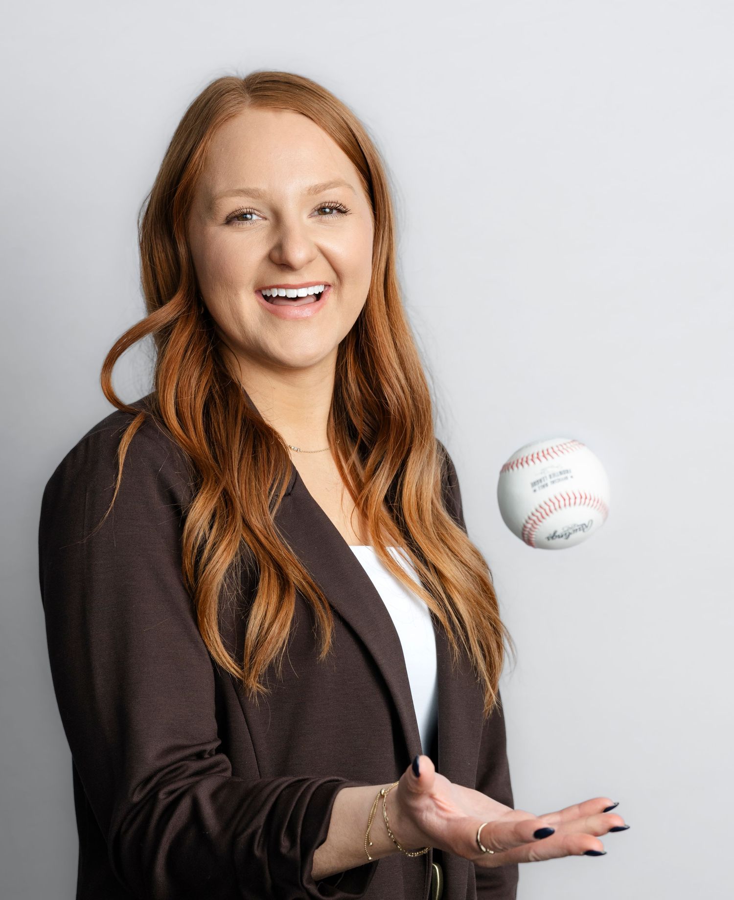 A series of professional headshots showing a person with red hair in a dark blazer posing with a baseball against a light background.
