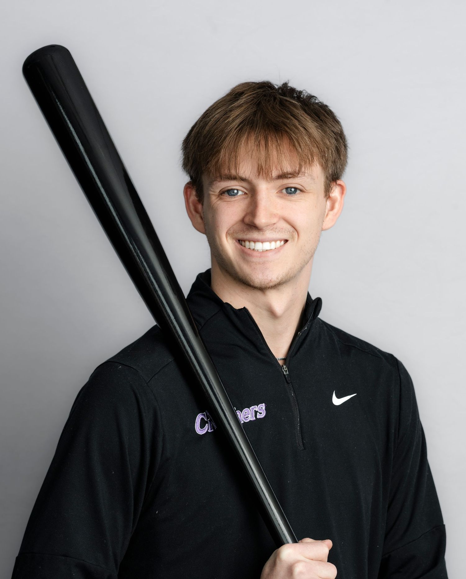 Baseball player in black Nike polo holds bat against white background in professional headshot series.