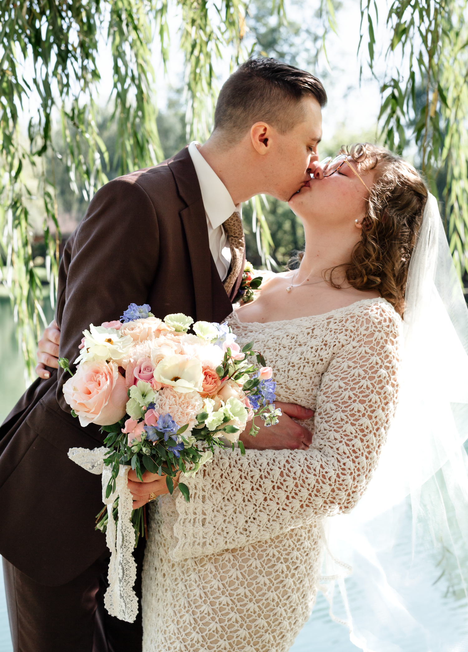 A romantic moment captured under willow trees with a beautiful floral bouquet.
