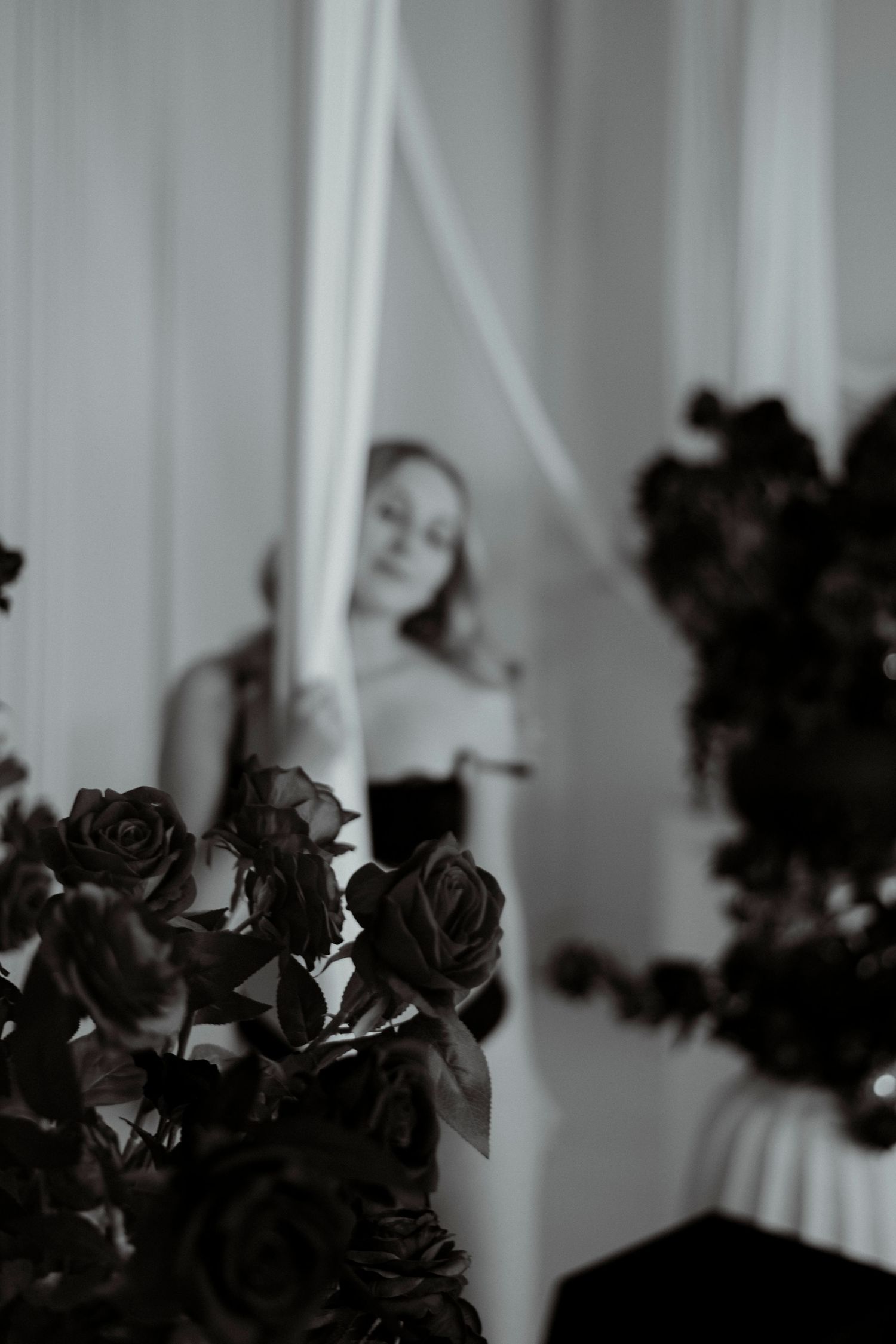 Dark silhouettes of roses against white curtains create a moody and dramatic window display.