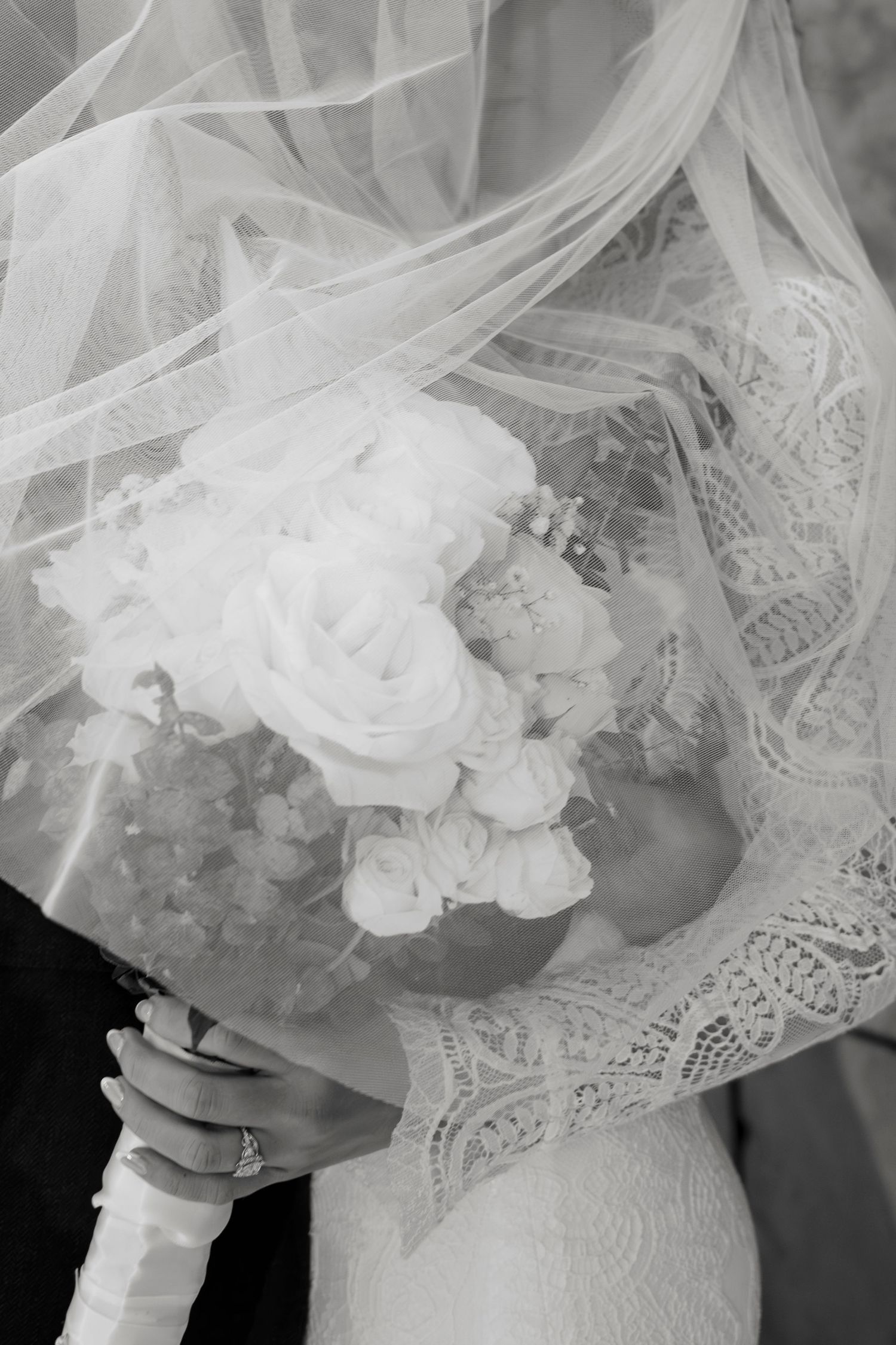 Delicate white lace veil and floral details create an ethereal bridal look in black and white photography.
