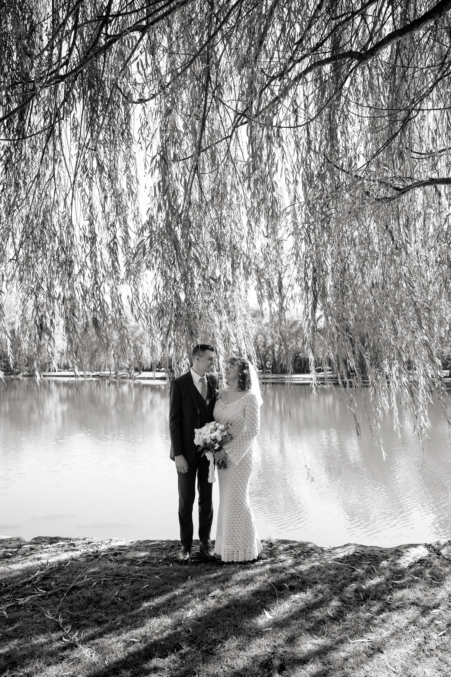 Black and white wedding portraits under weeping willow trees by a tranquil lake.