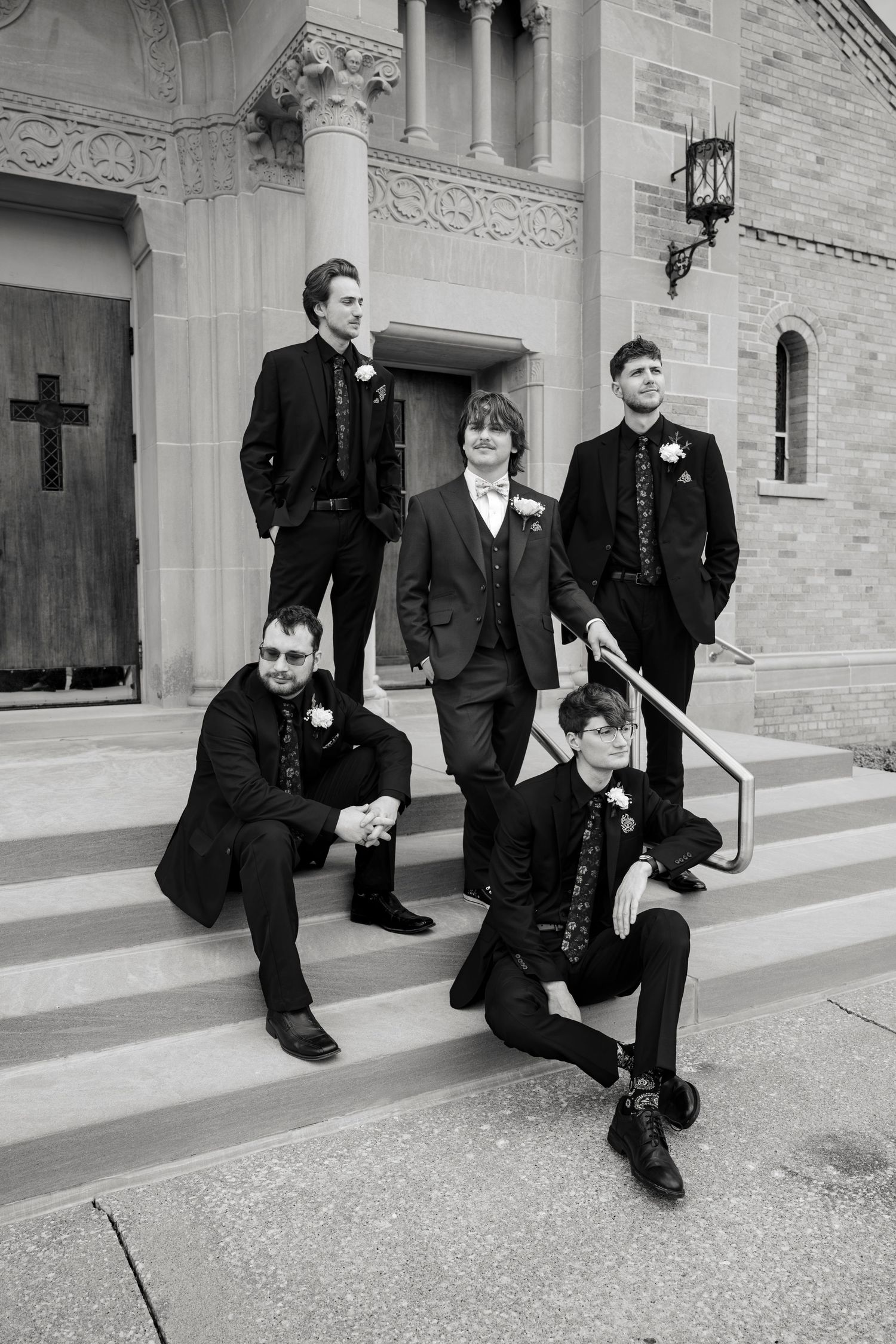 Five groomsmen in black suits pose on church steps in a classic black and white wedding portrait photo.