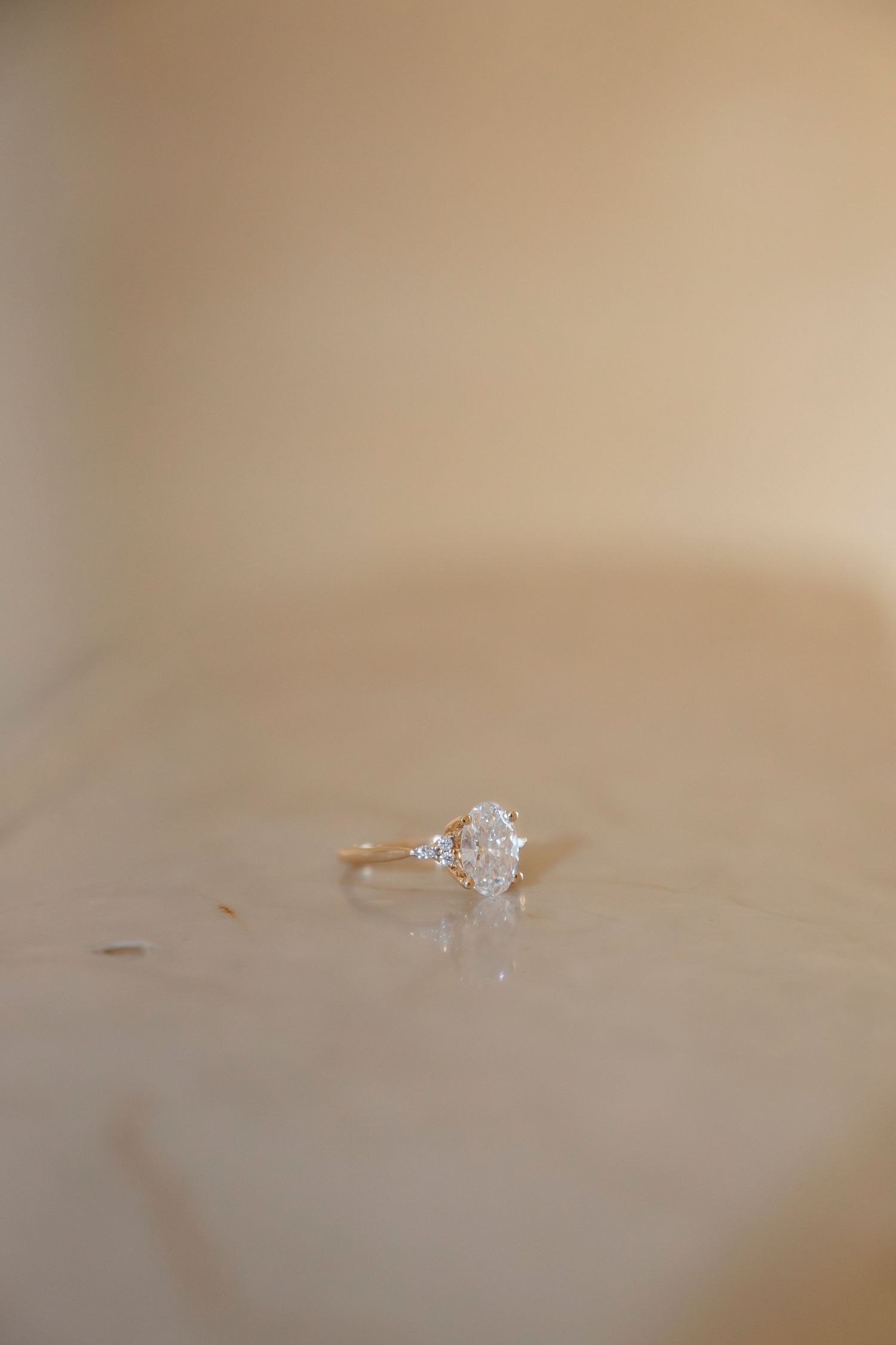 A delicate rose gold engagement ring with a pear-shaped diamond solitaire sits elegantly on a beige surface.