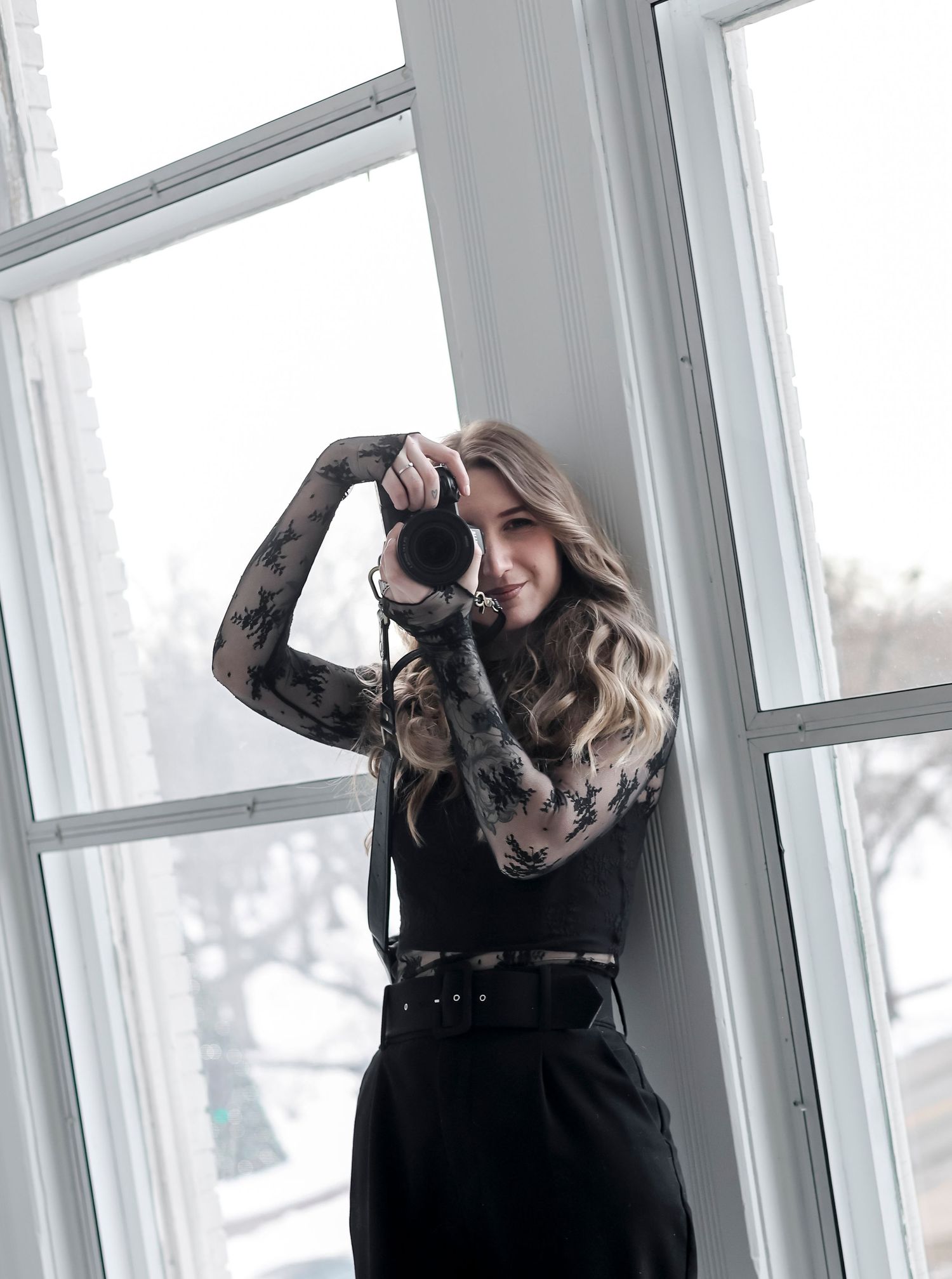 Woman in black dress posing against bright windows in a fashion photography series.