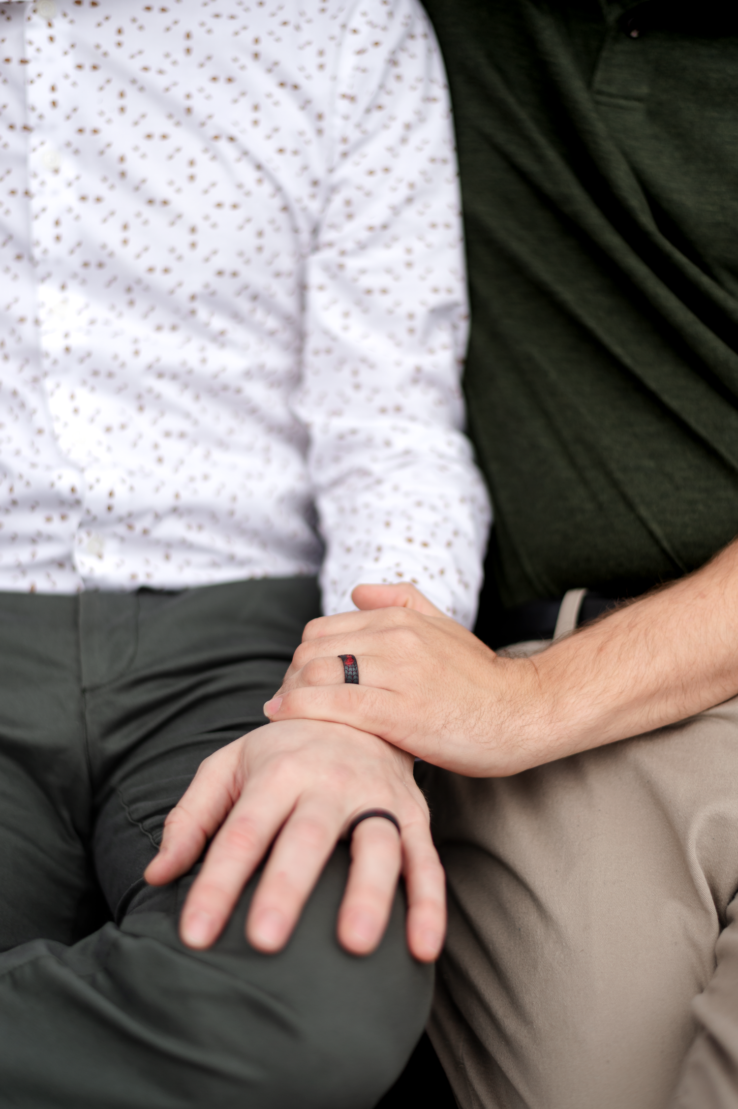 Close-up of two people sitting together, one wearing a black silicone ring, holding hands affectionately.