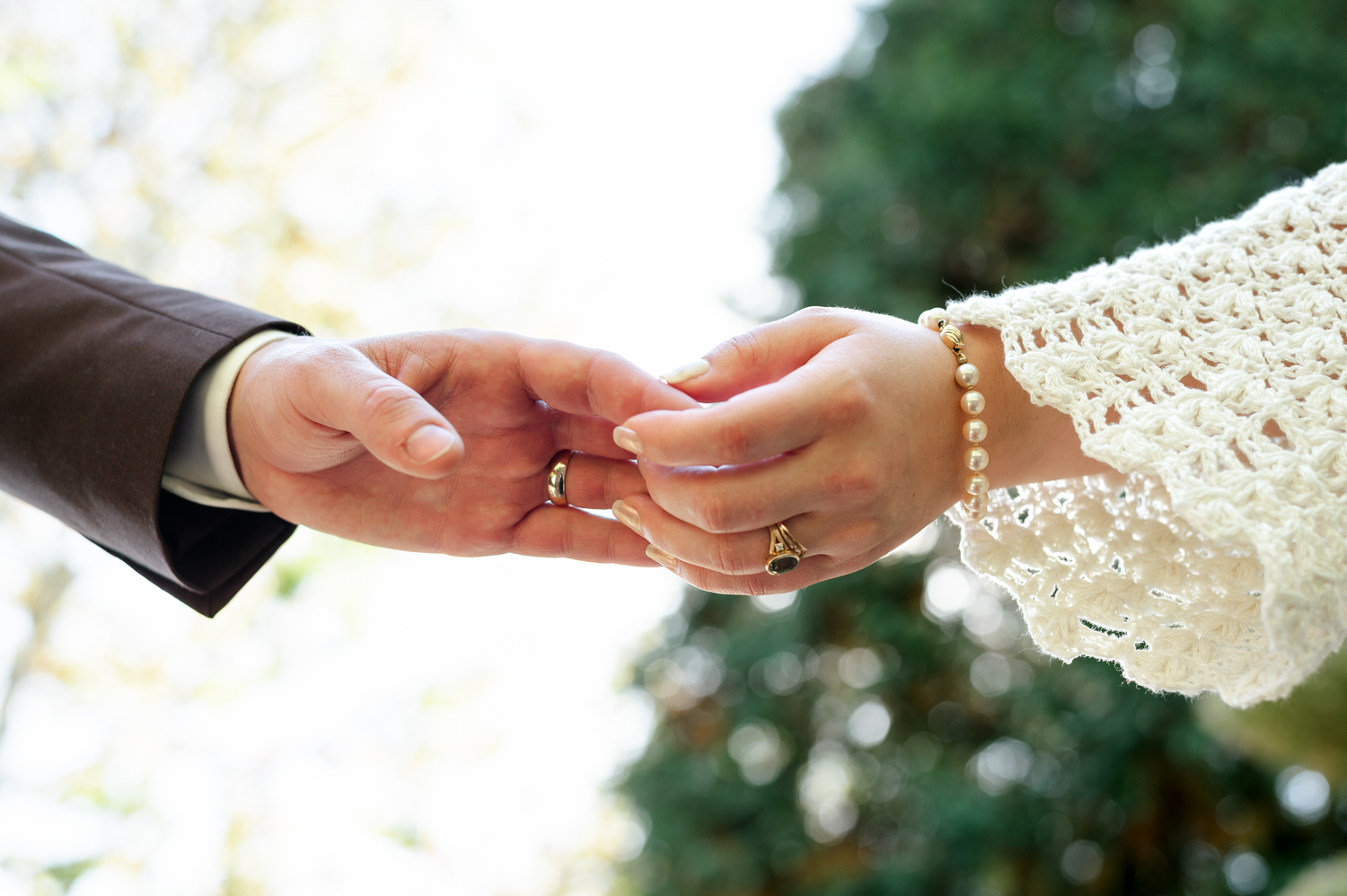 Close up of couple's hands exchanging rings during outdoor wedding ceremony.