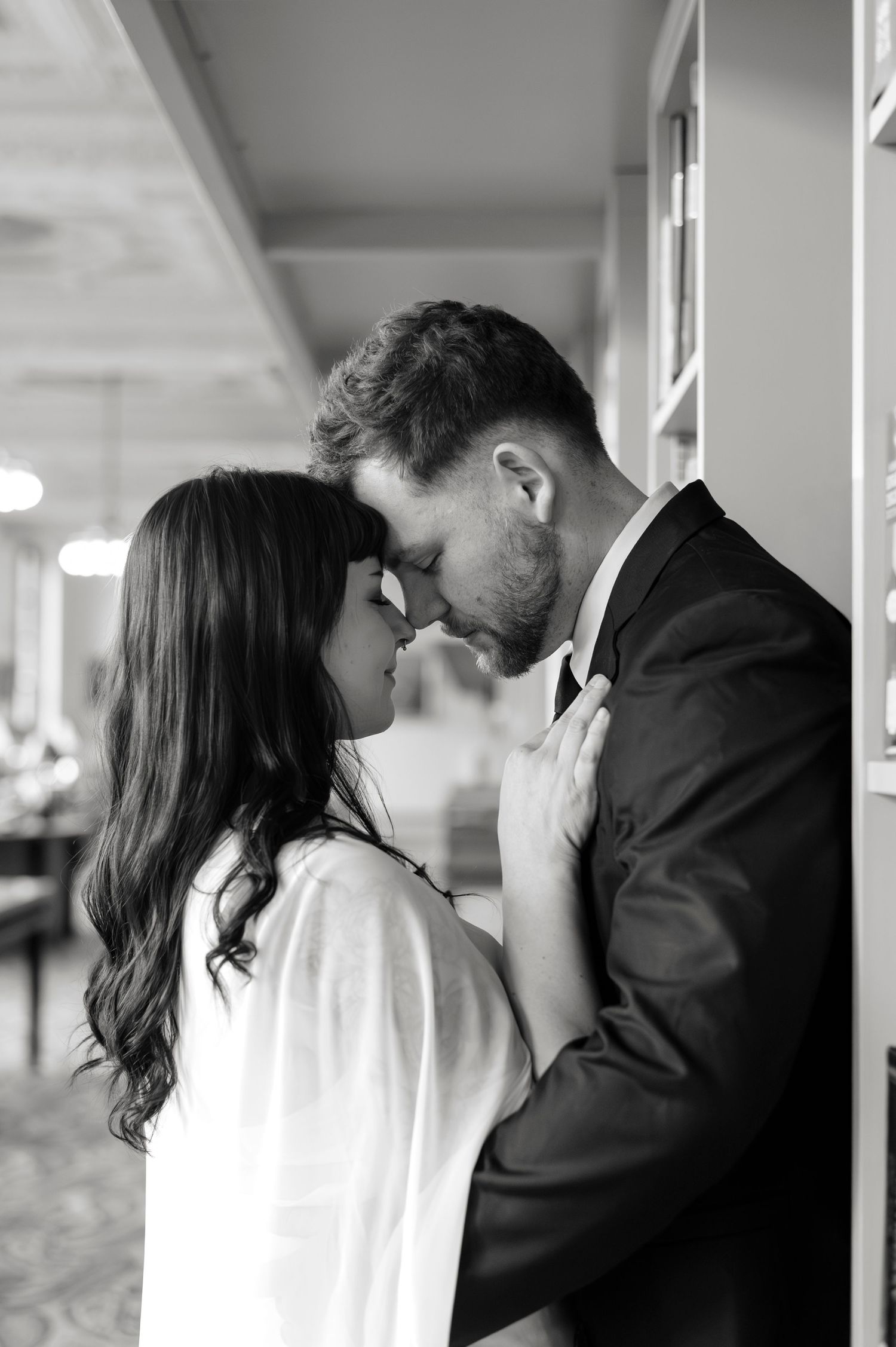 Black and white photo of a romantic couple leaning foreheads together tenderly indoors.