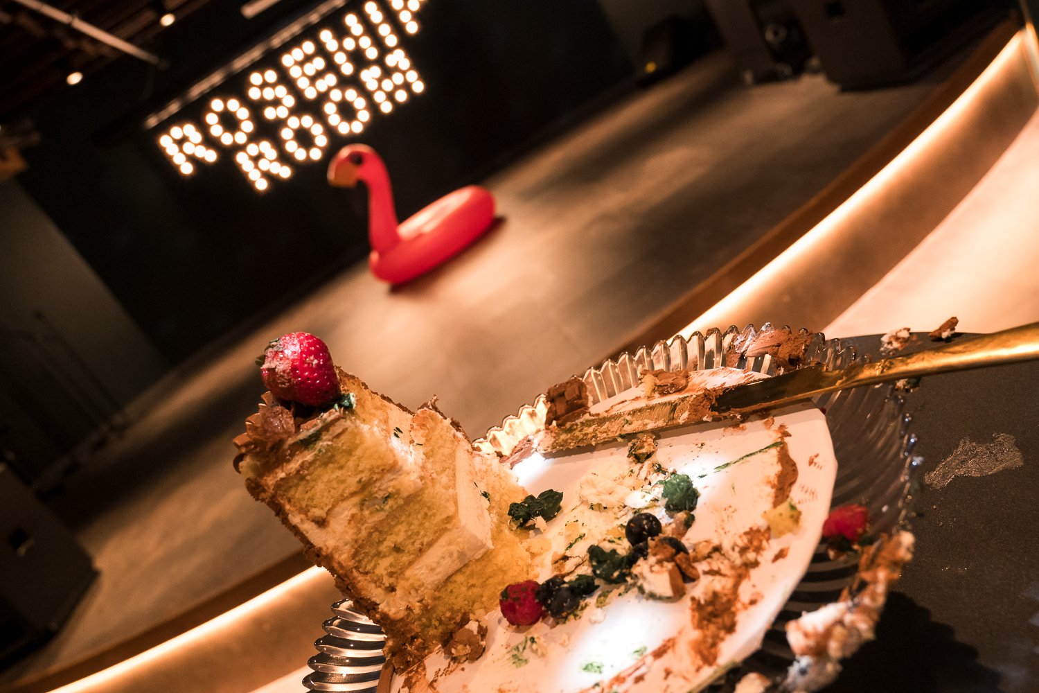 Chocolate cake with raspberry garnish being sliced on dark wooden table in dim restaurant lighting.