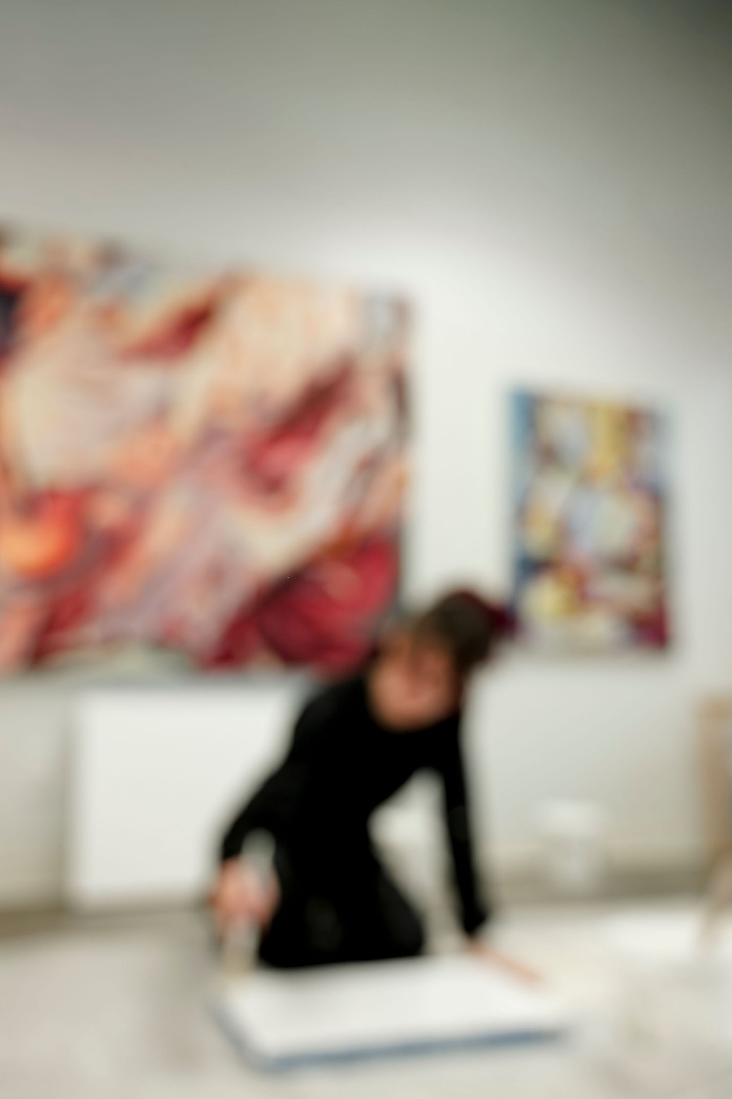 Blurred gallery space with abstract paintings hanging on white walls.