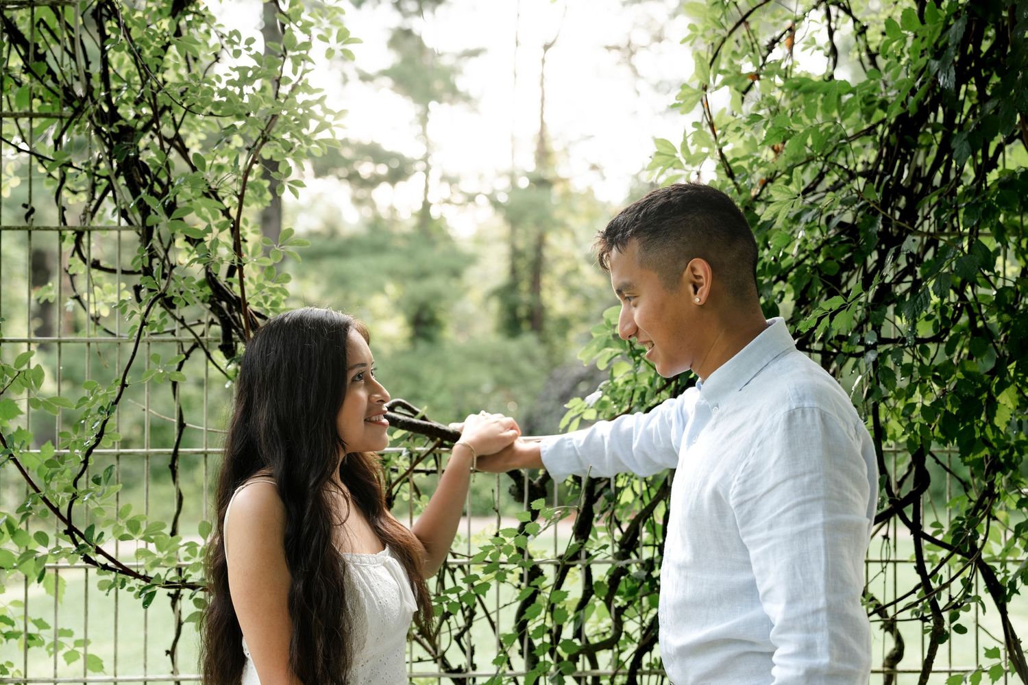 Couple holding hands among lush green ivy vines outdoors, sharing a romantic moment in a garden setting.
